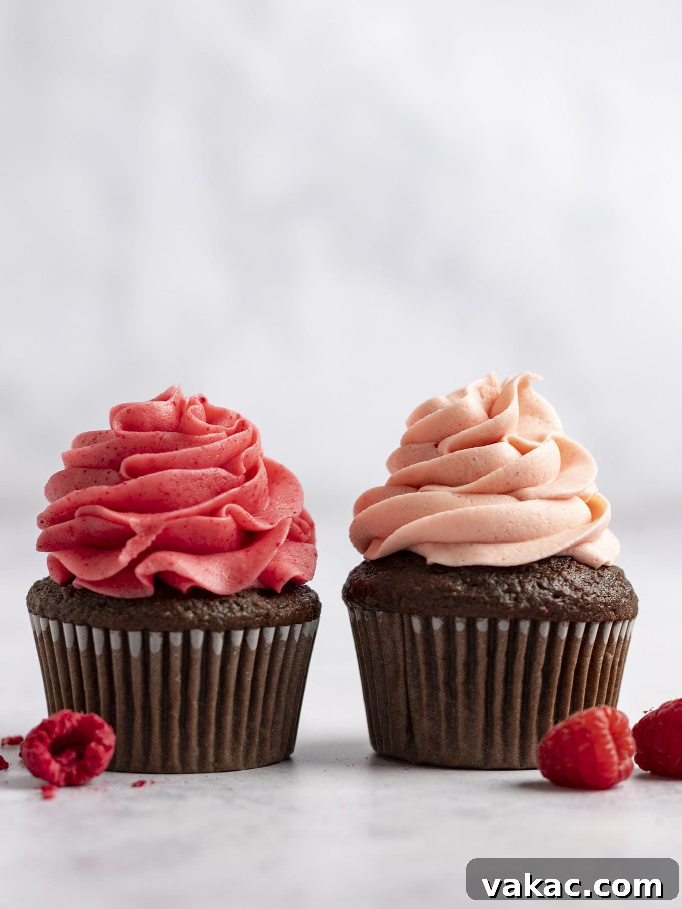 Velvet Raspberry Icing 14 Two chocolate cupcakes, each topped with a different version of raspberry frosting, sitting side by side. The left cupcake has frosting made with freeze-dried raspberries, appearing more vibrant. The right cupcake has frosting made with fresh raspberries, displaying a slightly lighter hue.