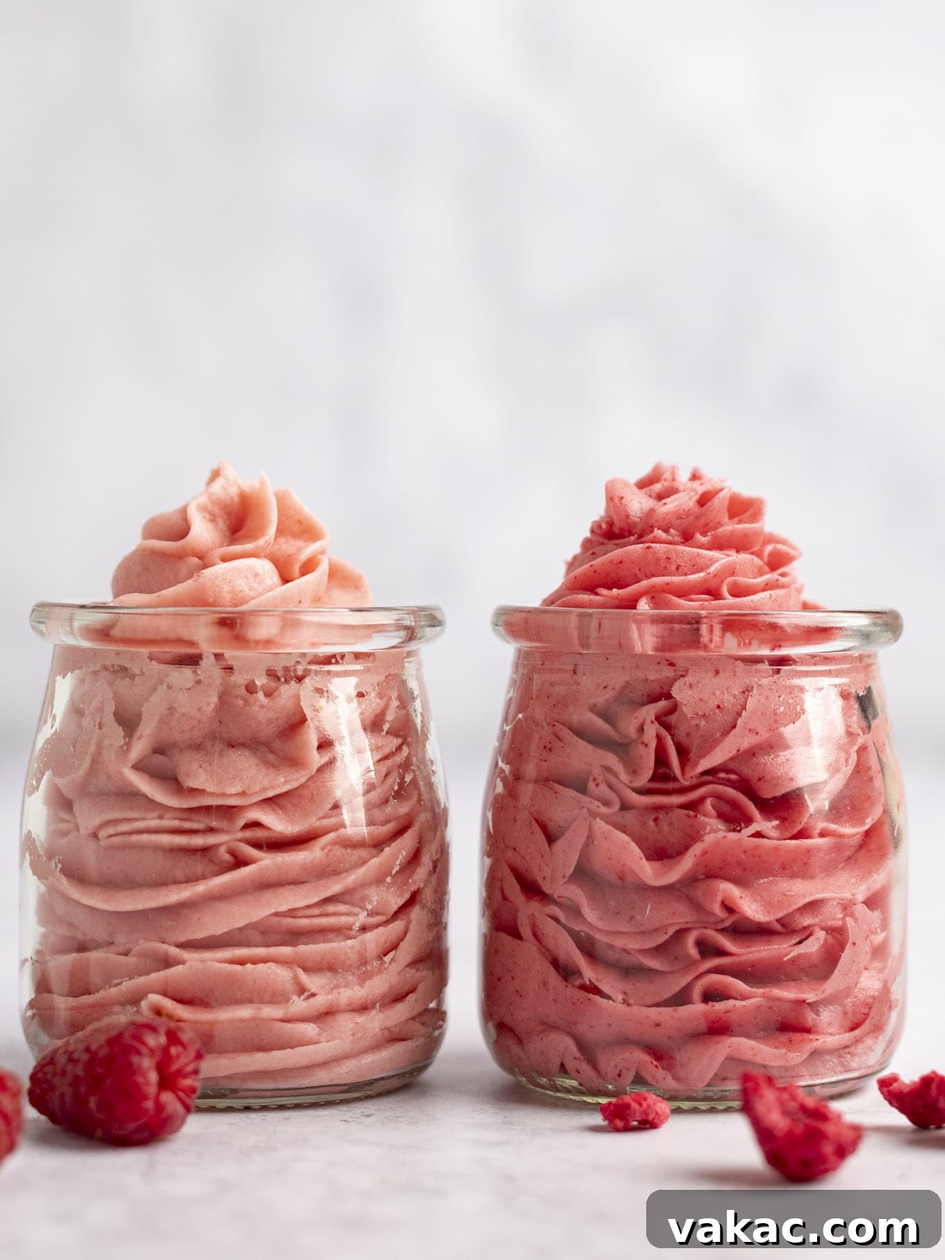 Velvet Raspberry Icing 15 Two glass jars filled with raspberry frosting. The jar on the left contains frosting made with fresh raspberries, while the jar on the right holds frosting made with freeze-dried raspberries, highlighting their color difference.