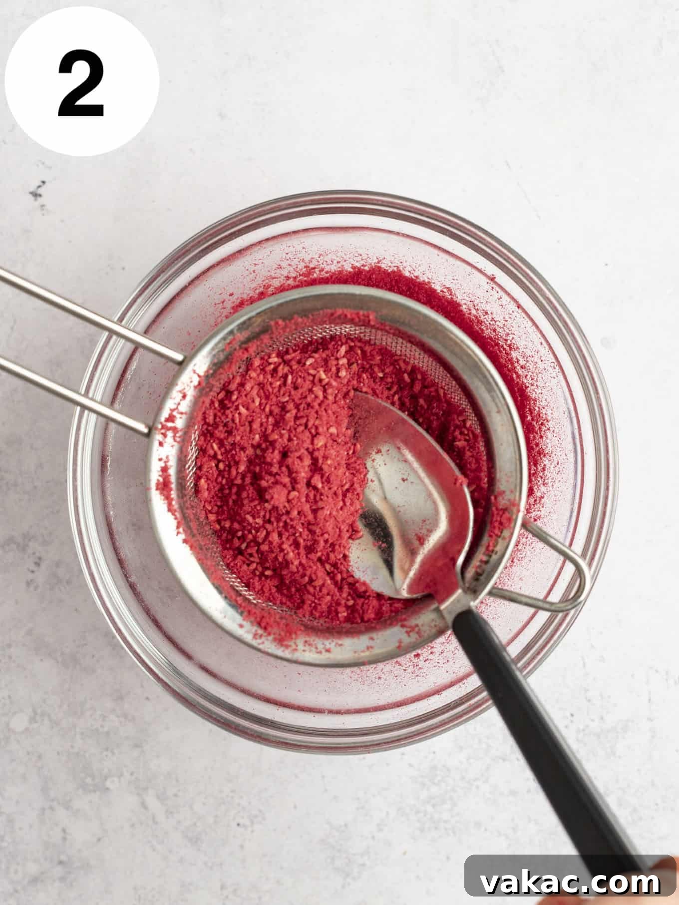 Velvet Raspberry Icing 5 An overhead view of freeze-dried raspberry powder being carefully passed through a fine mesh sieve to remove seeds, ensuring a smooth frosting.