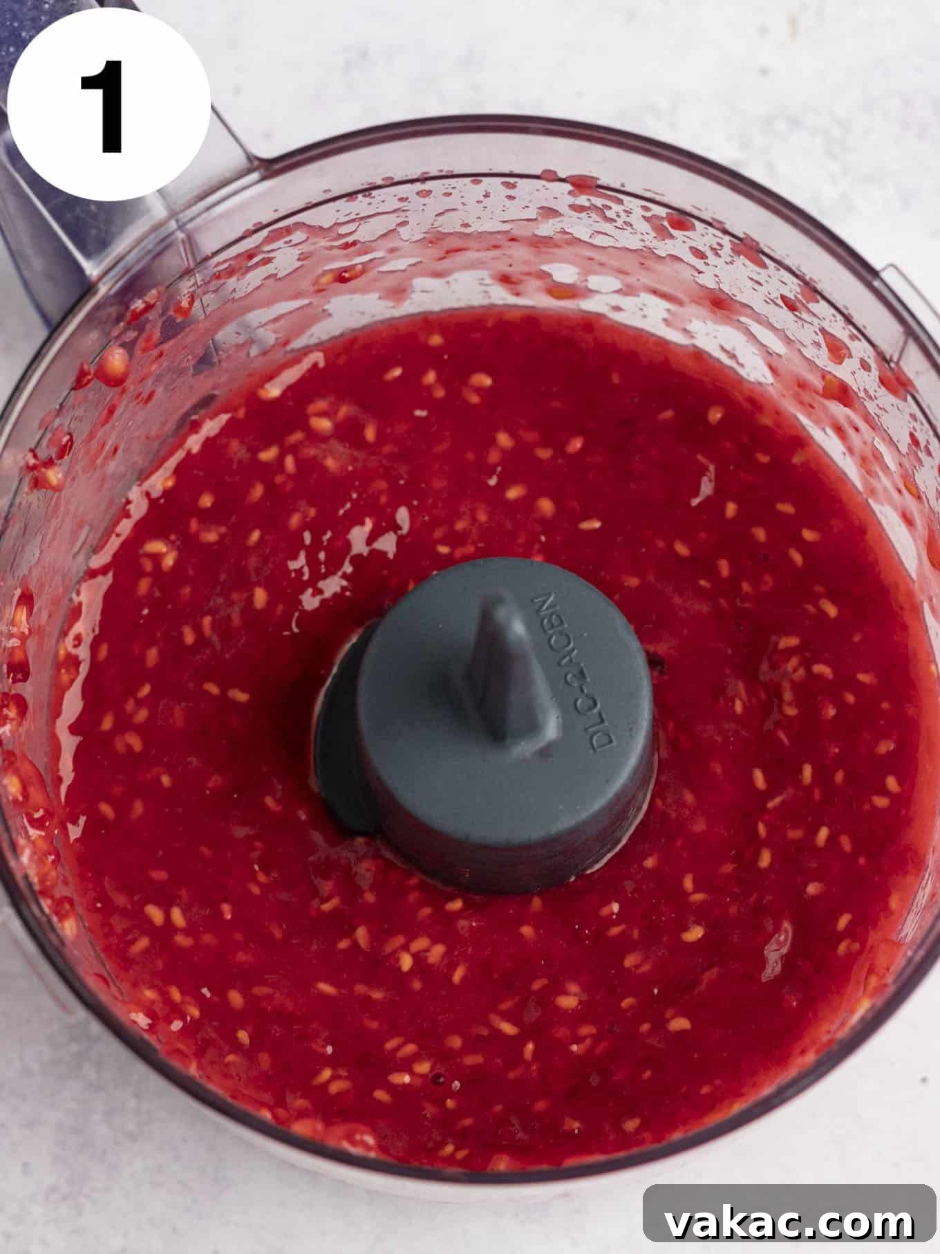 Velvet Raspberry Icing 8 An overhead view of smooth, bright red pureed raspberries in the bowl of a food processor, ready for straining.
