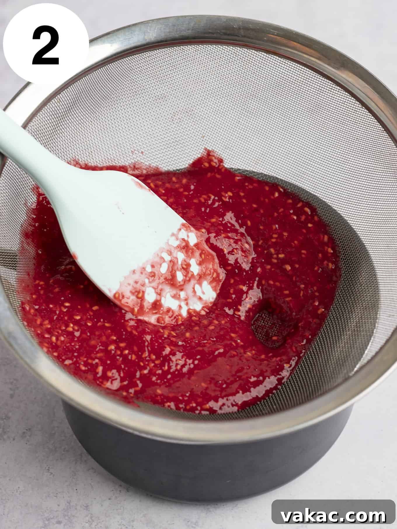 Velvet Raspberry Icing 9 An overhead view of fresh raspberry puree being pressed through a fine mesh sieve to remove seeds, ensuring a smooth base for the frosting.