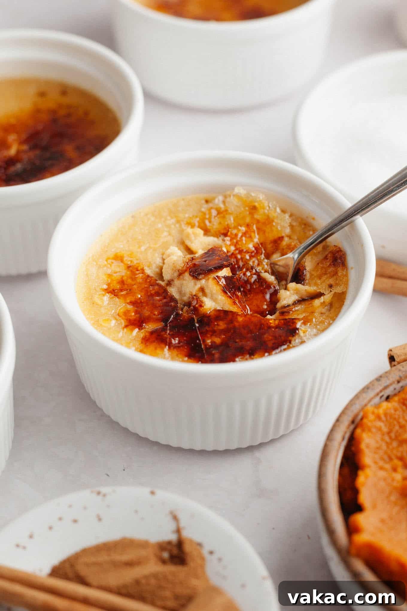 Spiced Pumpkin Creme Brulee 11 A ramekin of pumpkin crème brûlée with the golden, caramelized sugar topping perfectly cracked open by a spoon, ready to be enjoyed.