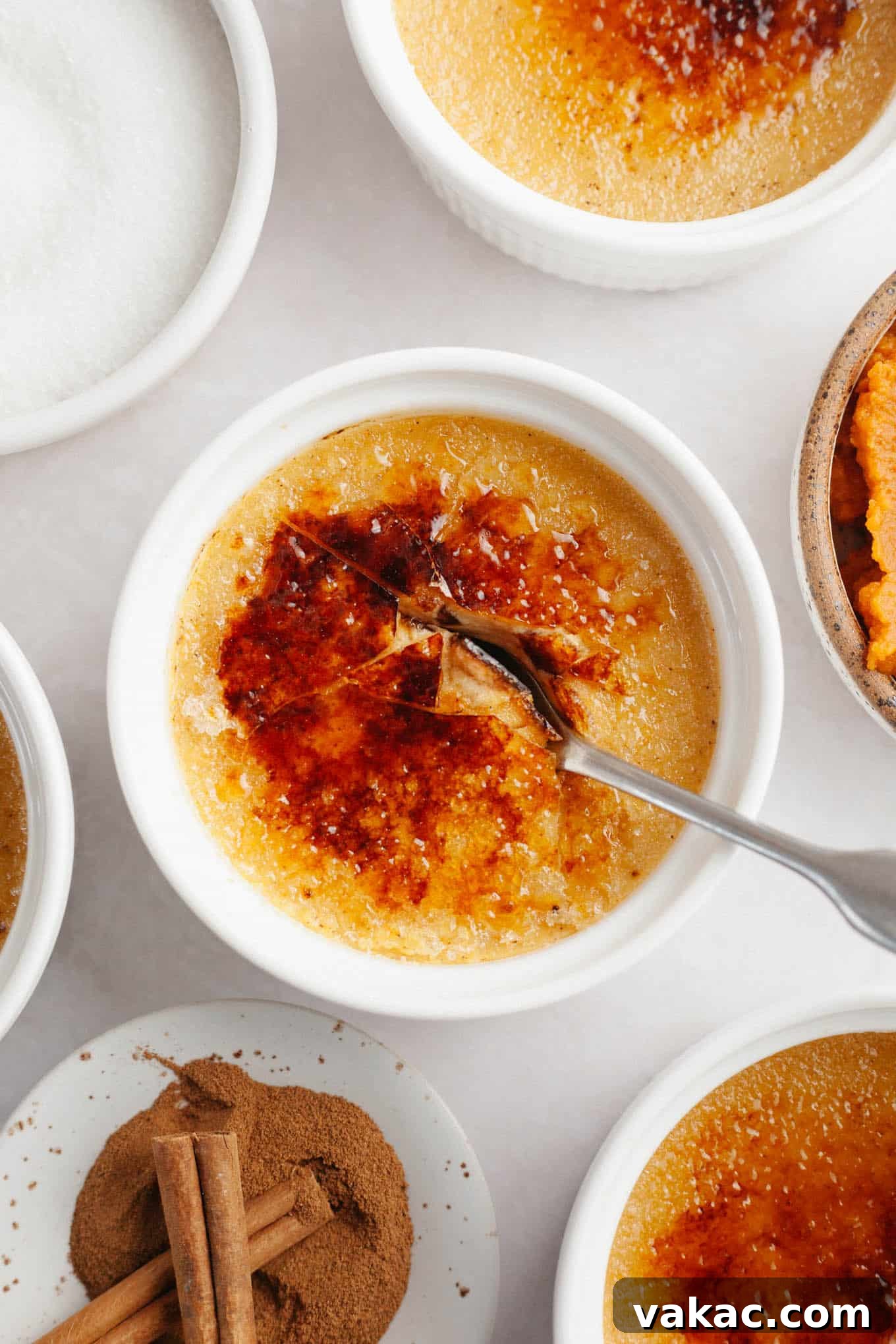 Spiced Pumpkin Creme Brulee 10 An overhead view of a spoon breaking through the caramelized sugar topping of a pumpkin crème brûlée, revealing the creamy custard beneath.
