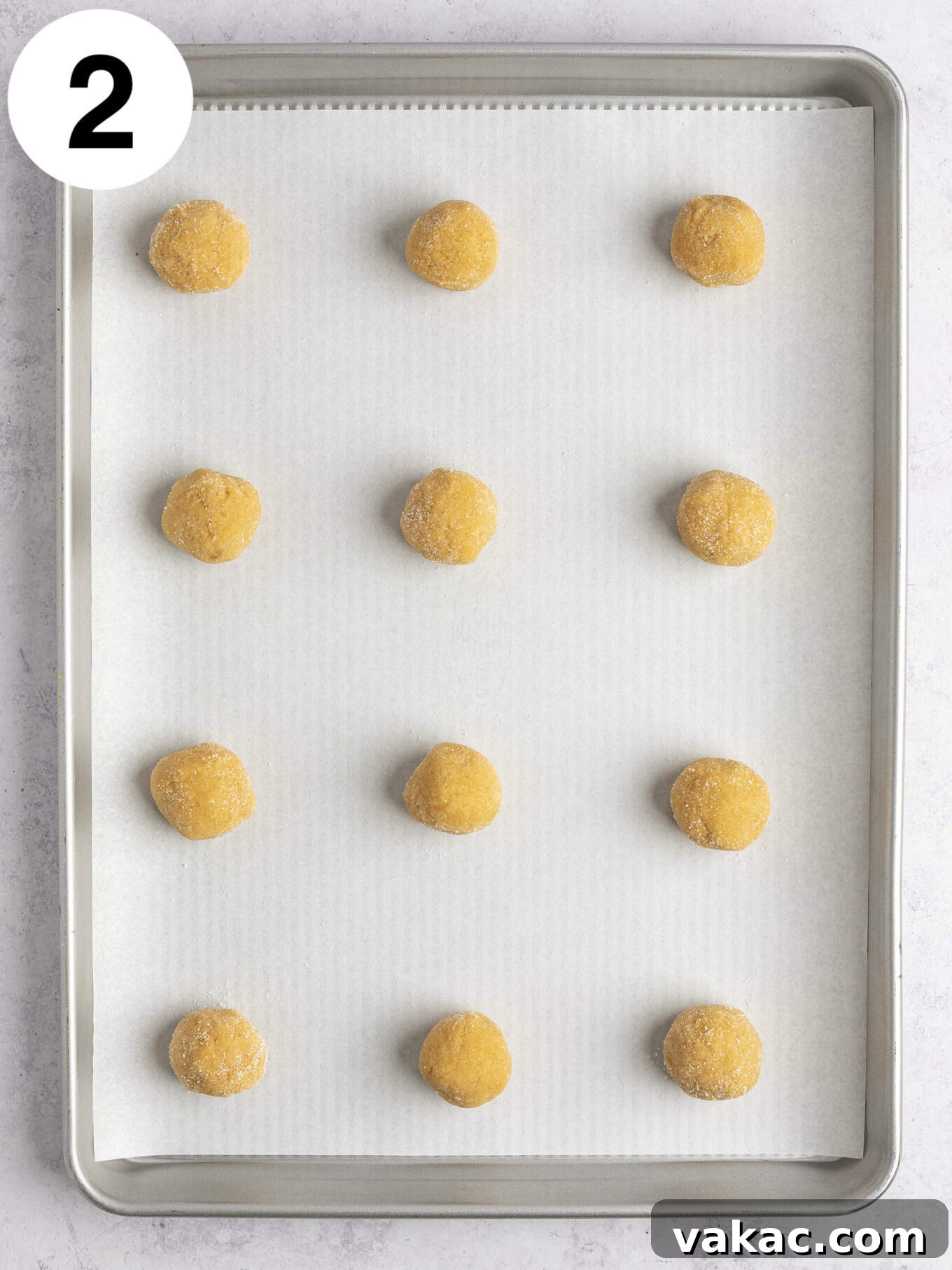 An overhead view of peanut butter cookie dough balls on a parchment paper-lined baking sheet.