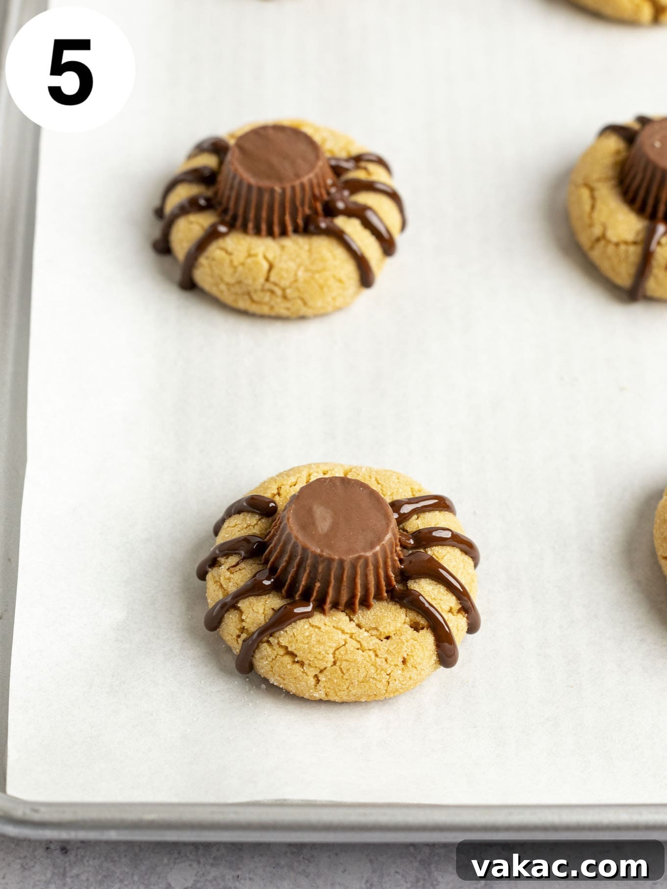 A process shot showing peanut butter cup cookies with spider legs piped onto them with melted chocolate.