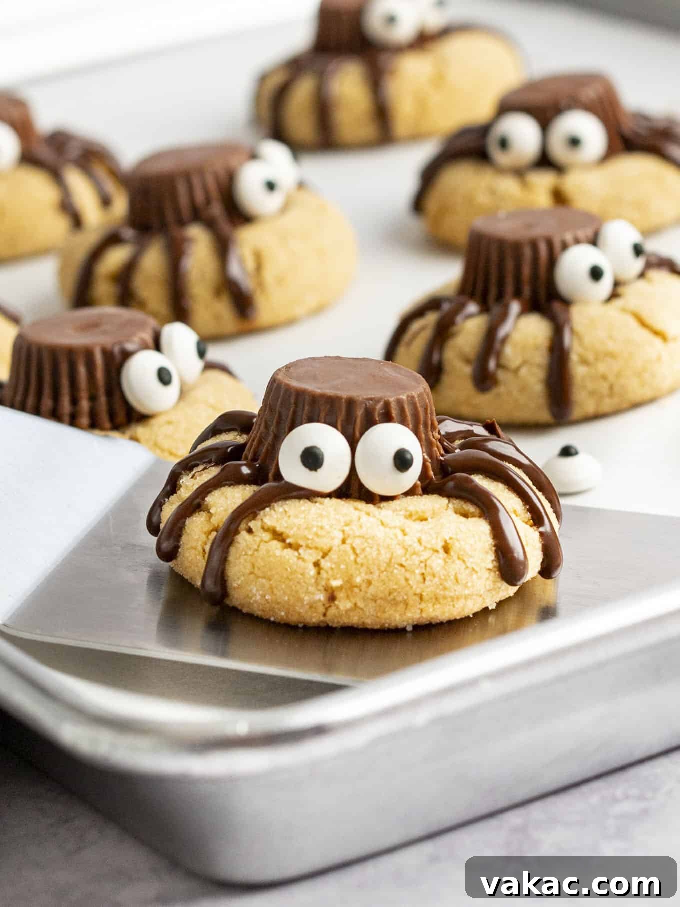 A spider cookie with candy eyes being lifted off a baking sheet.