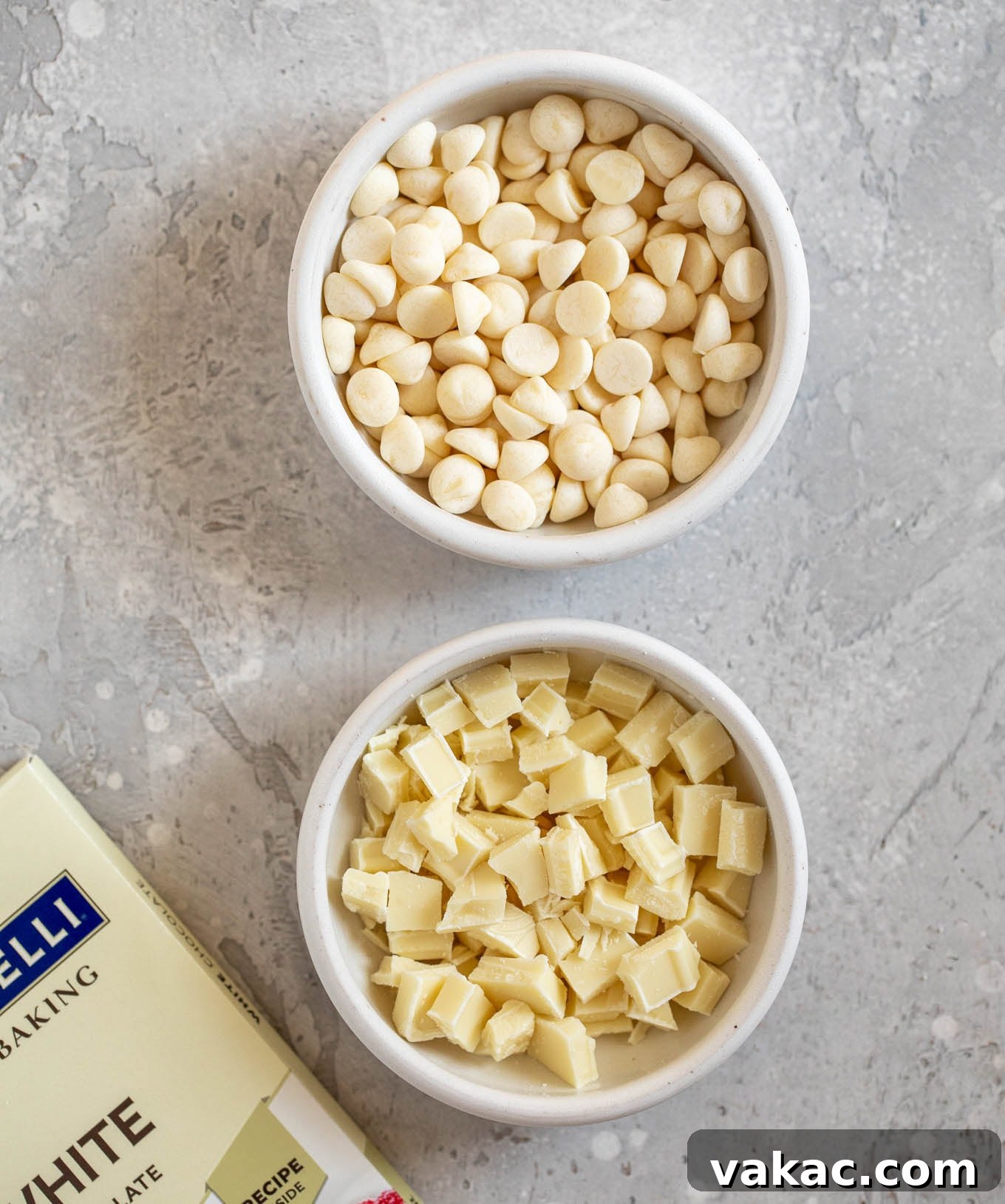 Velvet White Chocolate Frosting 3 An overhead view of white chocolate chips and finely chopped white chocolate bars in separate white bowls, highlighting the difference in form.