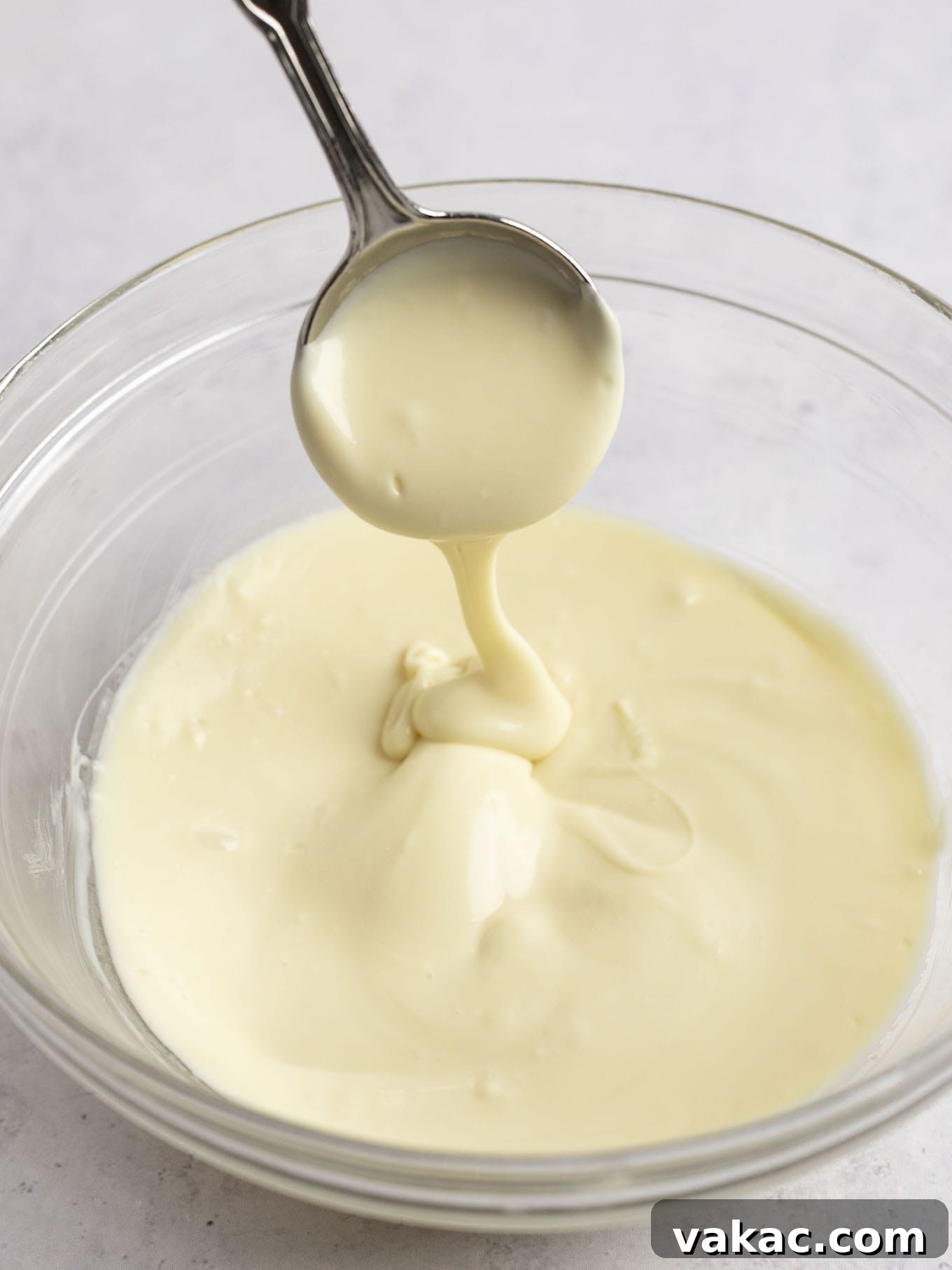 Velvet White Chocolate Frosting 4 A bowl of perfectly melted white chocolate with a spoon resting in it, showcasing its smooth, glossy texture.