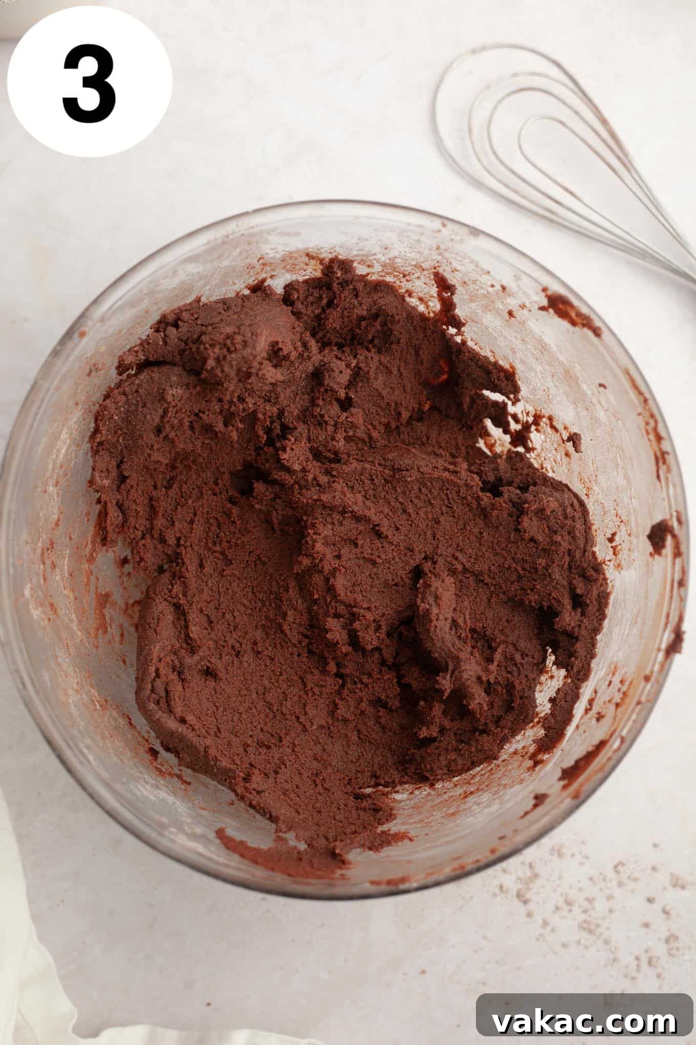 An overhead view of chocolate cookie dough in a glass mixing bowl.