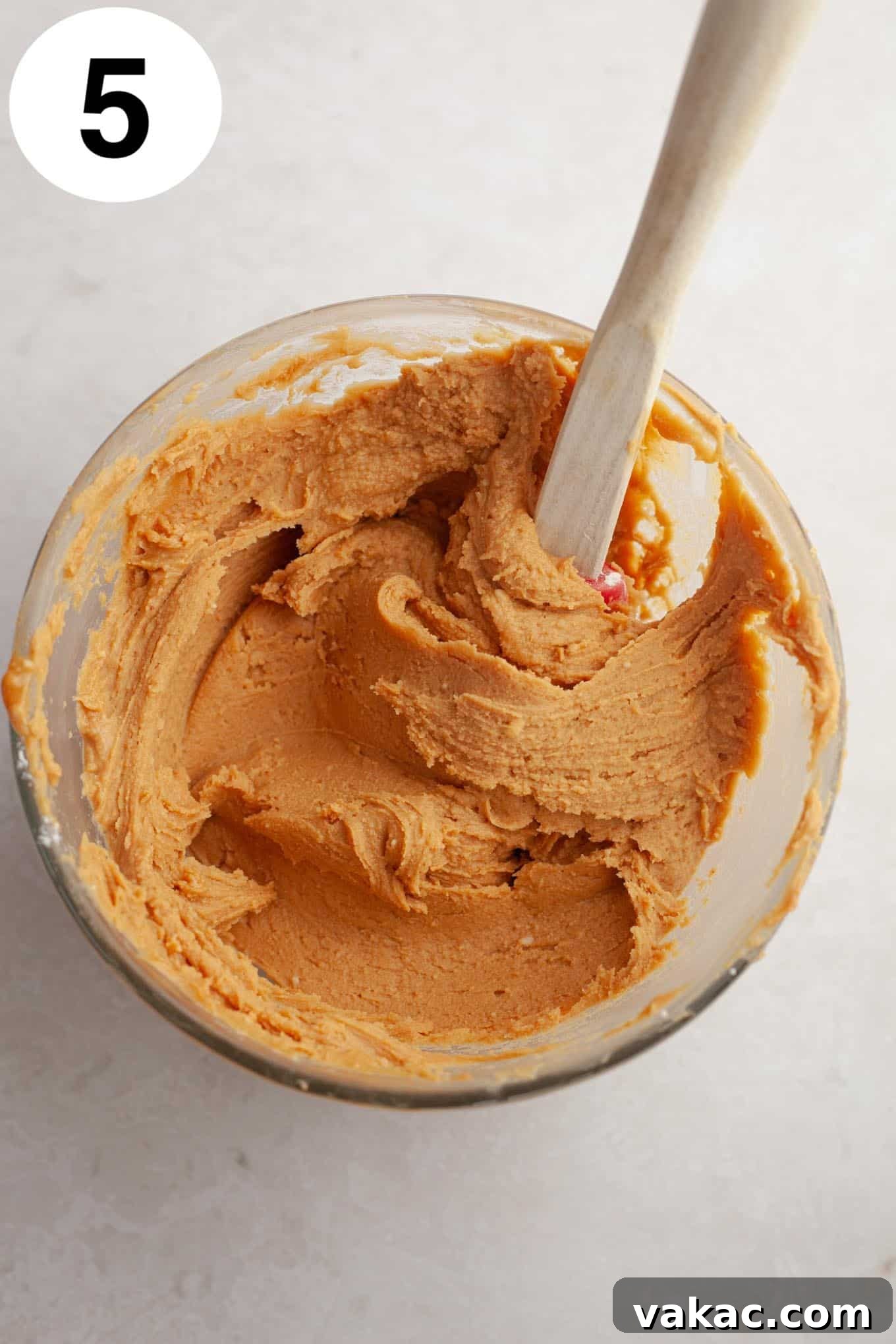 An overhead view of a peanut butter fudge mixture in a glass mixing bwol, with a spatula.
