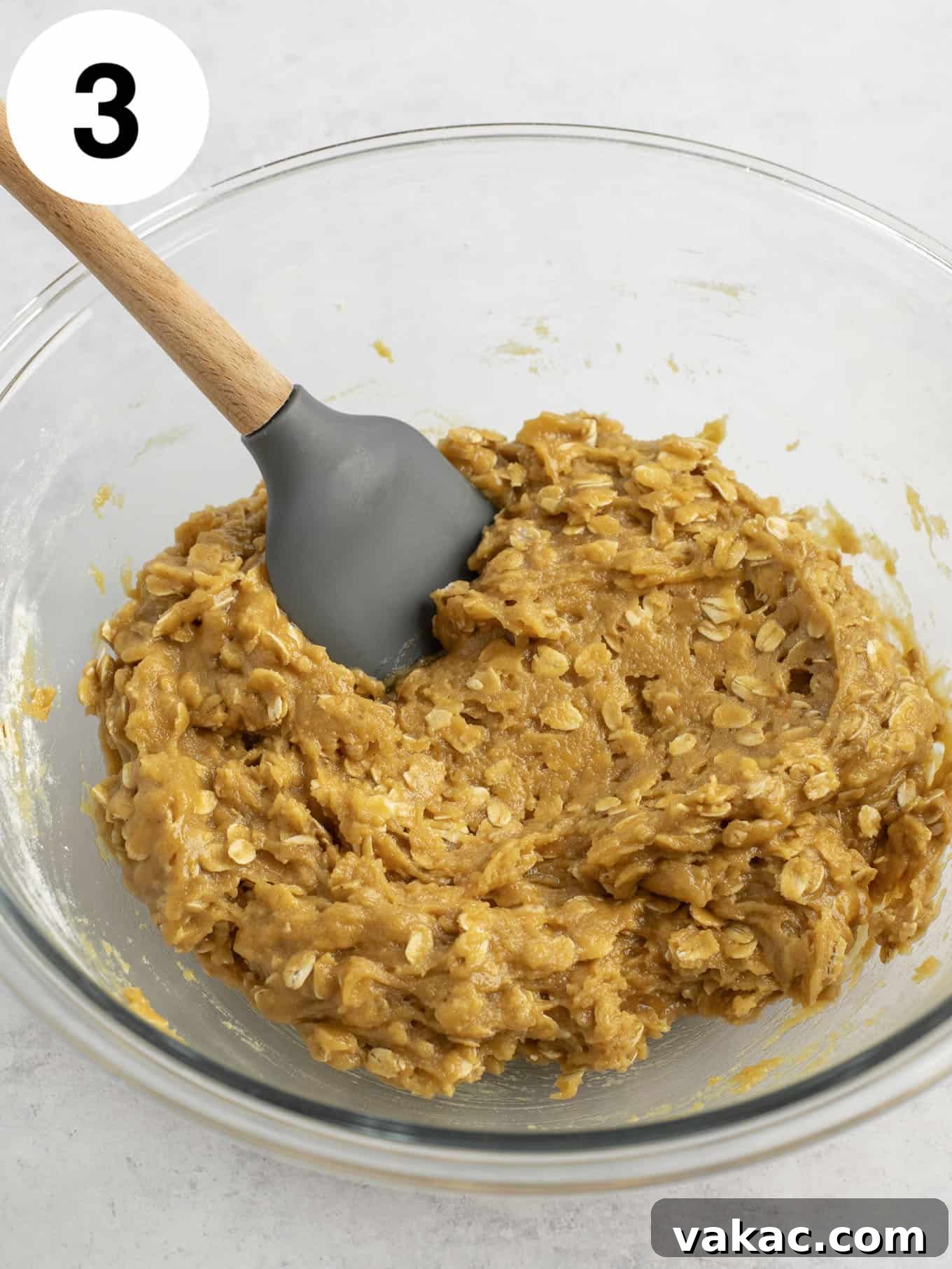 Ultimate Everything Cookie Bars 6 Peanut butter oatmeal cookie dough in a glass mixing bowl, just after dry ingredients have been added, being gently stirred with a rubber spatula.