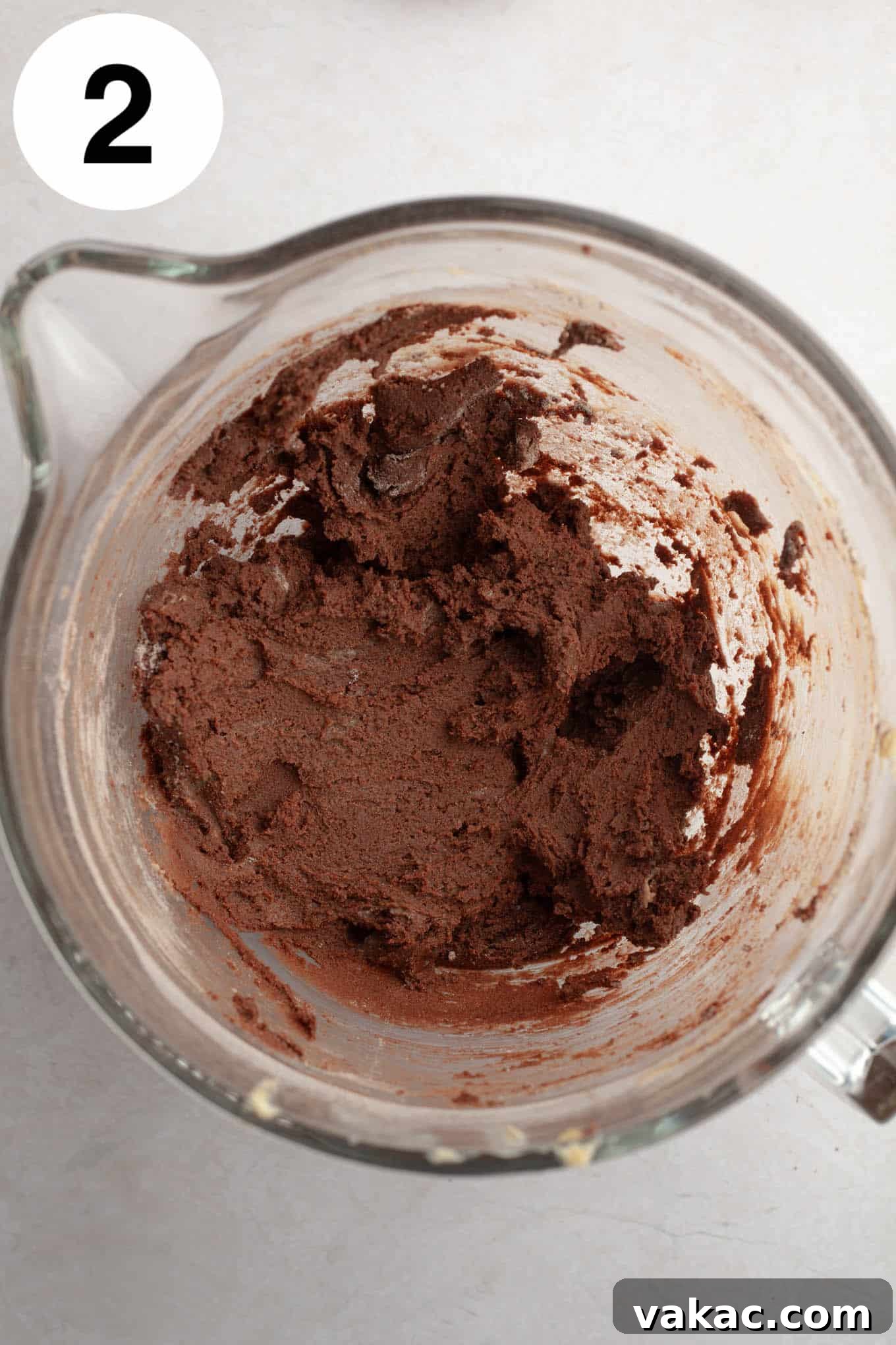 Decadent Chocolate Thumbprint Delights 5 An overhead view of rich chocolate cookie dough in a glass mixing bowl, showcasing its smooth texture.