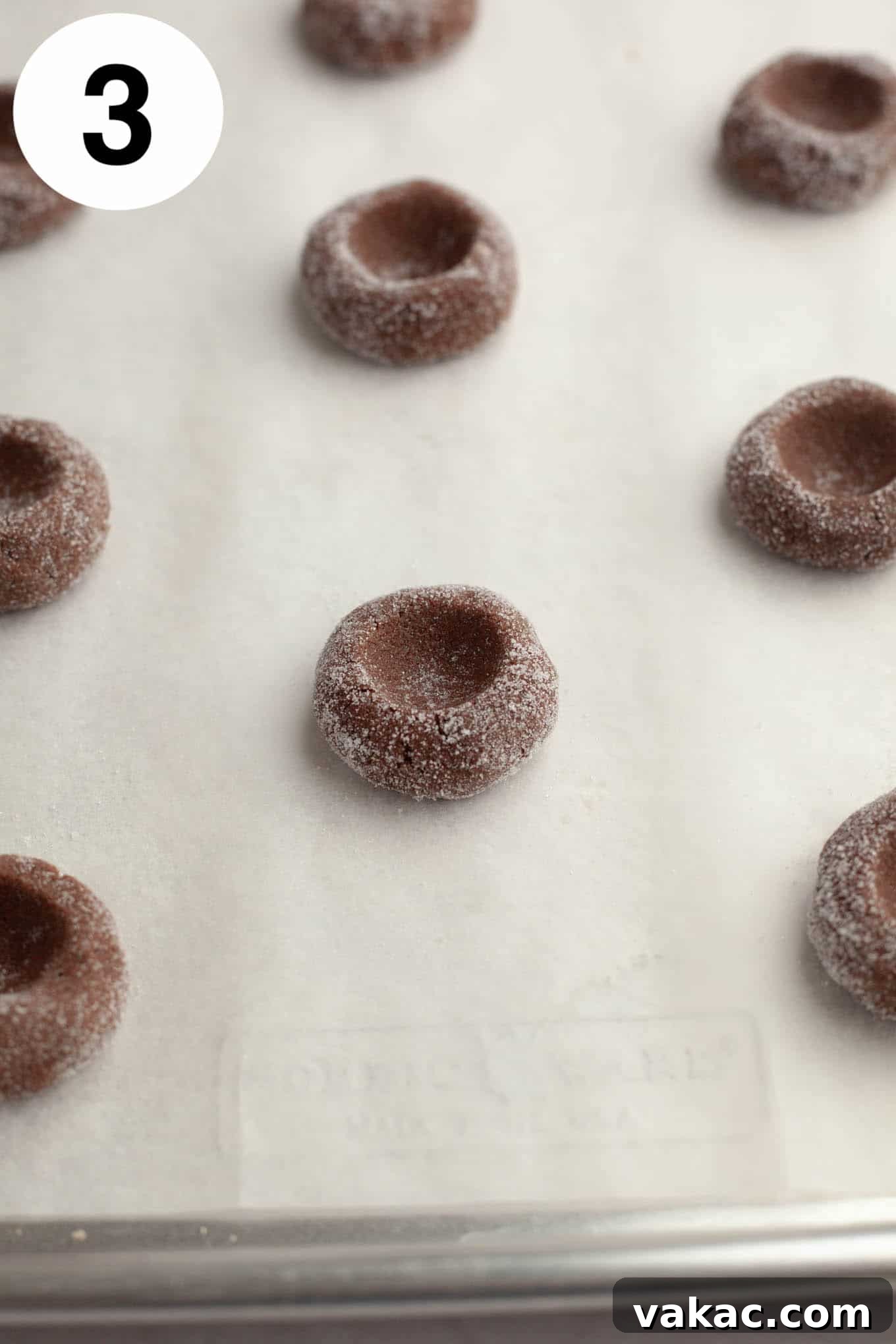 Decadent Chocolate Thumbprint Delights 6 Unbaked and unfilled chocolate thumbprints, perfectly rolled and indented, on a parchment-lined baking sheet.