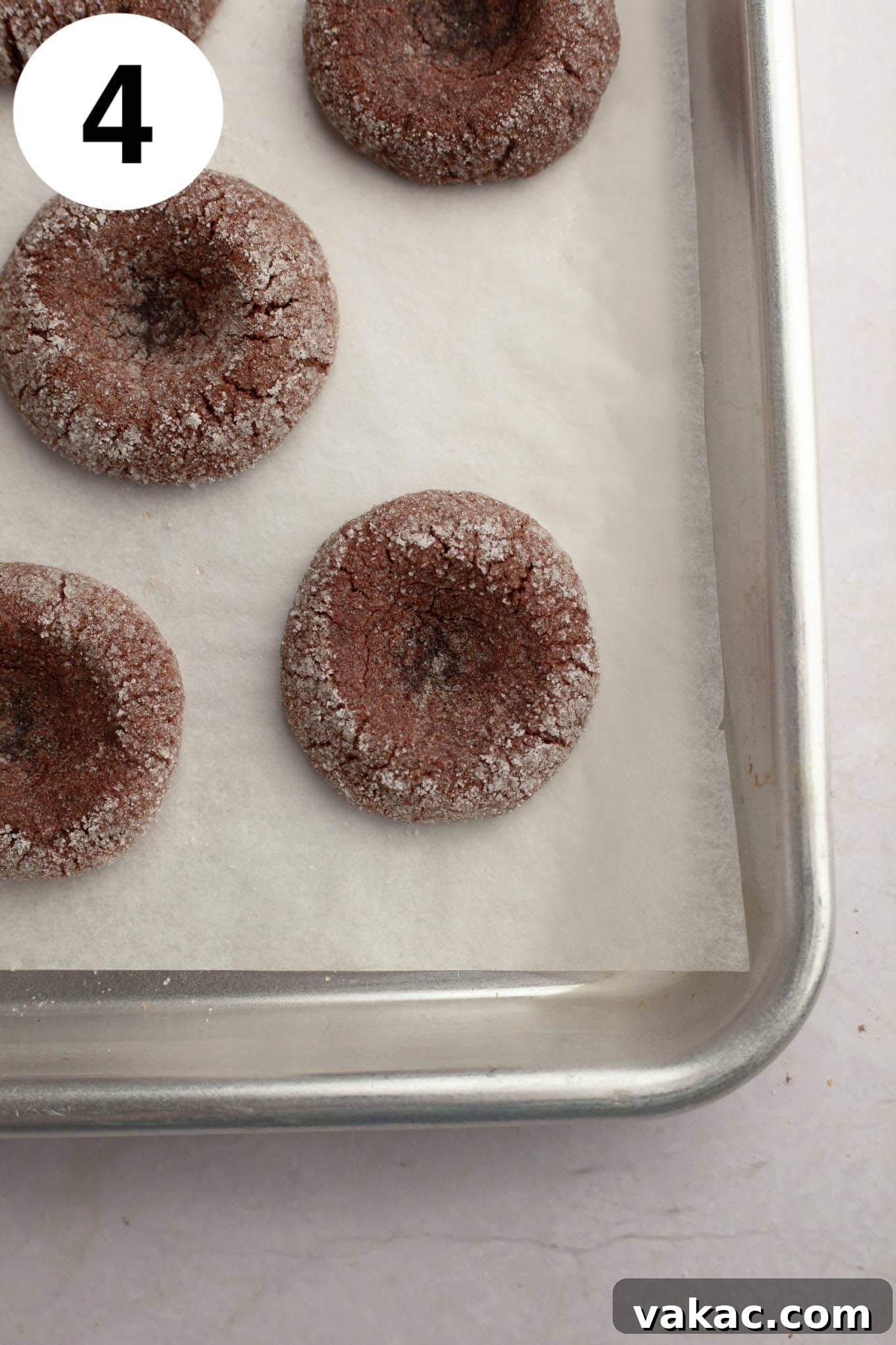 Decadent Chocolate Thumbprint Delights 7 Freshly baked and unfilled chocolate thumbprint cookies, showing slight indentations, cooling on a parchment-lined baking sheet.