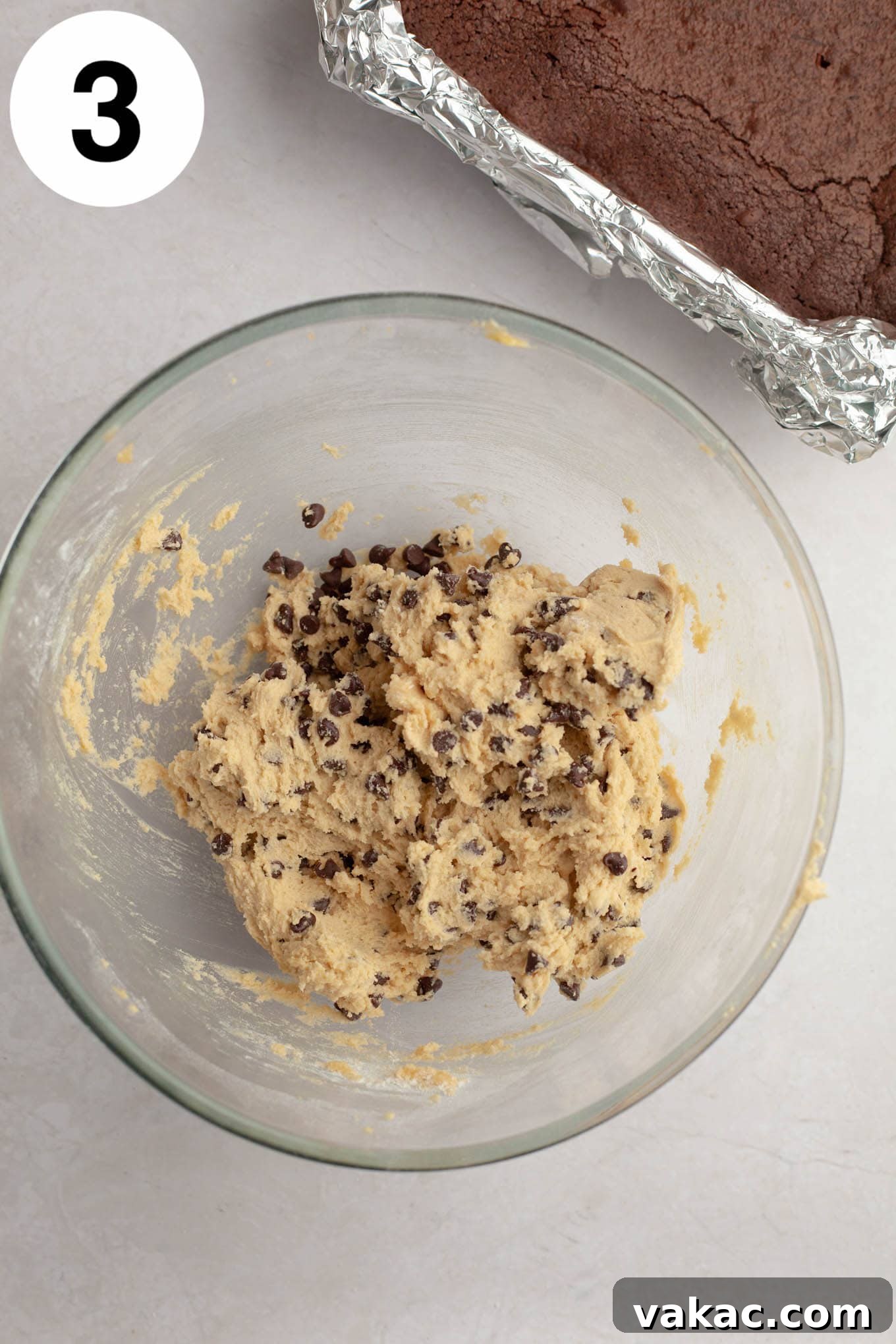 Brownie Cookie Dough Perfection 6 An overhead view of creamy, unbaked chocolate chip cookie dough in a glass mixing bowl, speckled with mini chocolate chips.