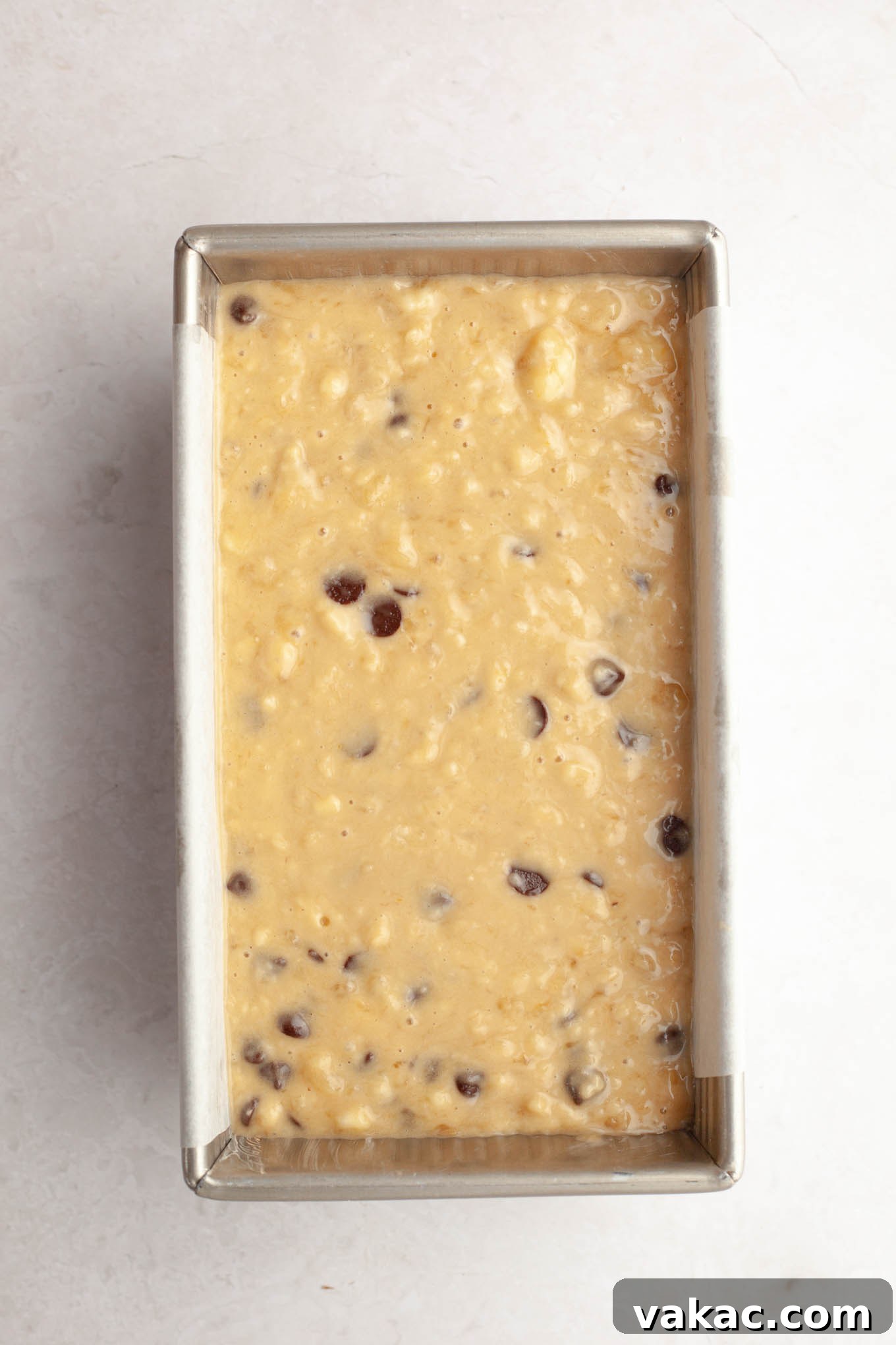 Decadent Chocolate Chip Banana Loaf 4 A loaf pan meticulously lined with parchment paper, containing smooth chocolate chip banana bread batter, ready for baking.