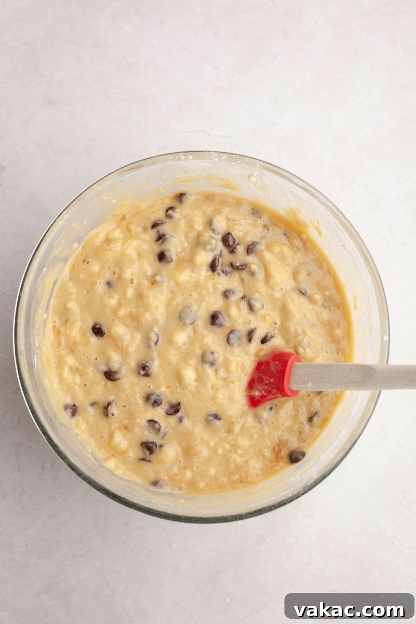 Decadent Chocolate Chip Banana Loaf 6 Chocolate chip banana bread batter in a clear glass mixing bowl, showing the consistency and distribution of chocolate chips before baking.
