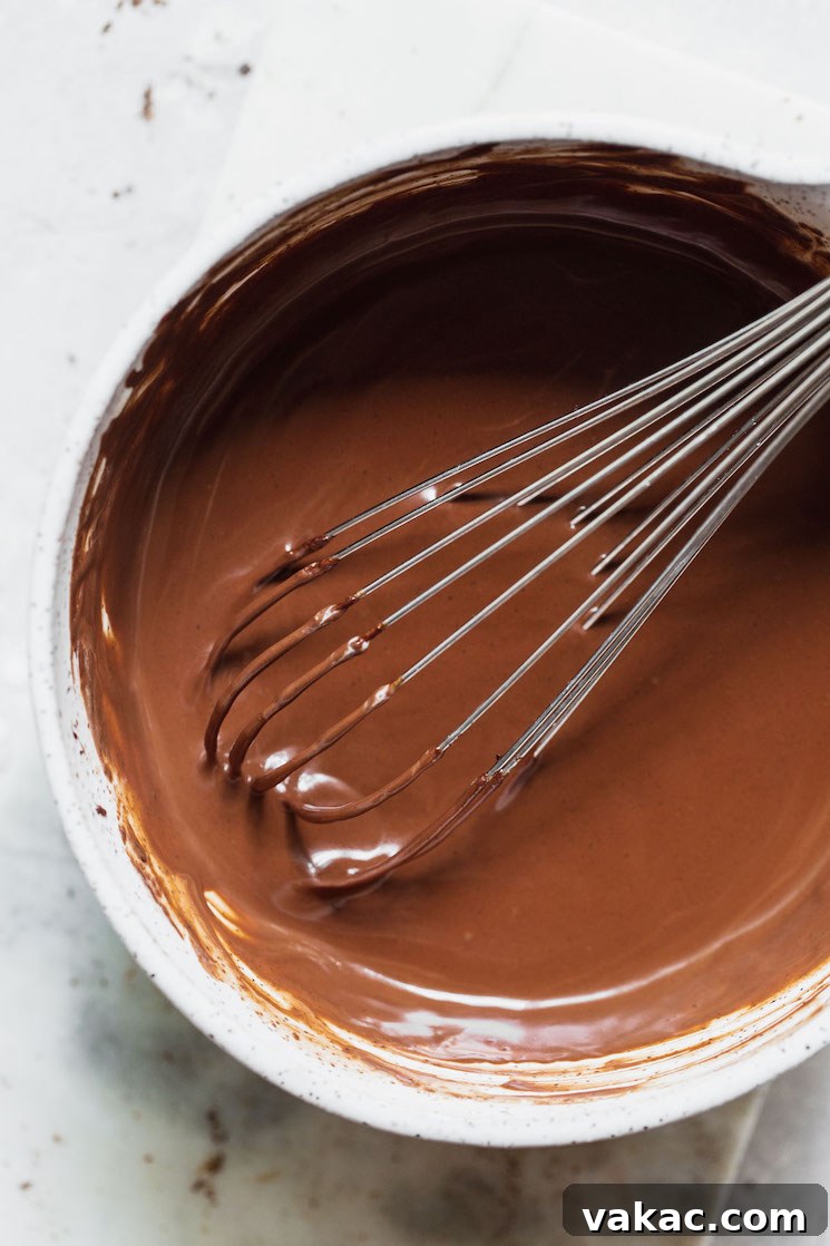 A pristine white mixing bowl filled with freshly prepared, smooth chocolate ganache, ready for use.