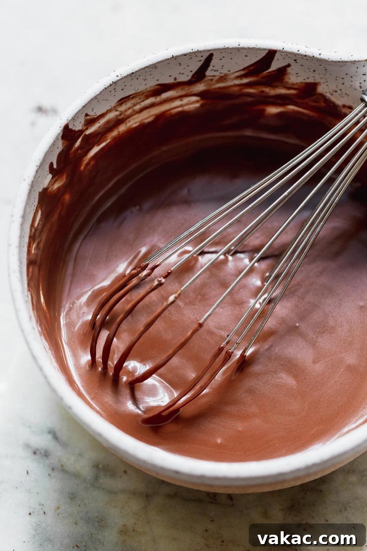 A white mixing bowl showcasing a beautifully smooth and glossy mixed chocolate ganache, perfectly emulsified.