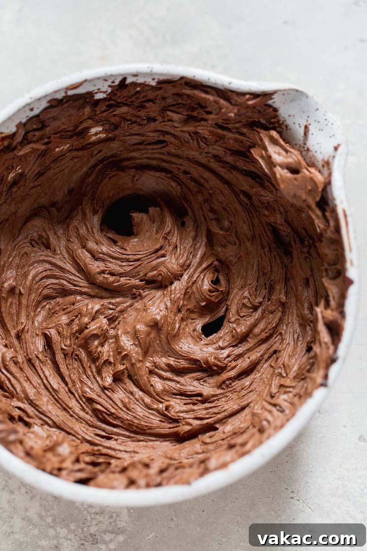 A white mixing bowl filled with rich chocolate ganache that has been expertly whipped, showcasing its lightened color and fluffy texture, ideal for frosting.