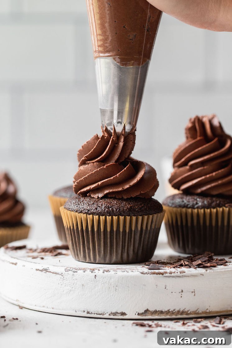 A rustic white wooden board topped with delicious chocolate cupcakes, each crowned with a generous swirl of fluffy whipped chocolate ganache frosting.