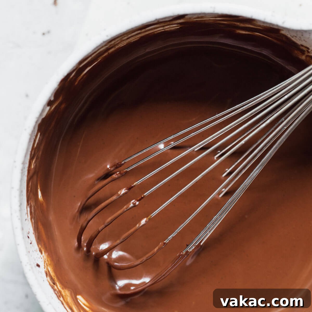 A white mixing bowl filled with beautifully mixed chocolate ganache, highlighting its smooth and rich texture.