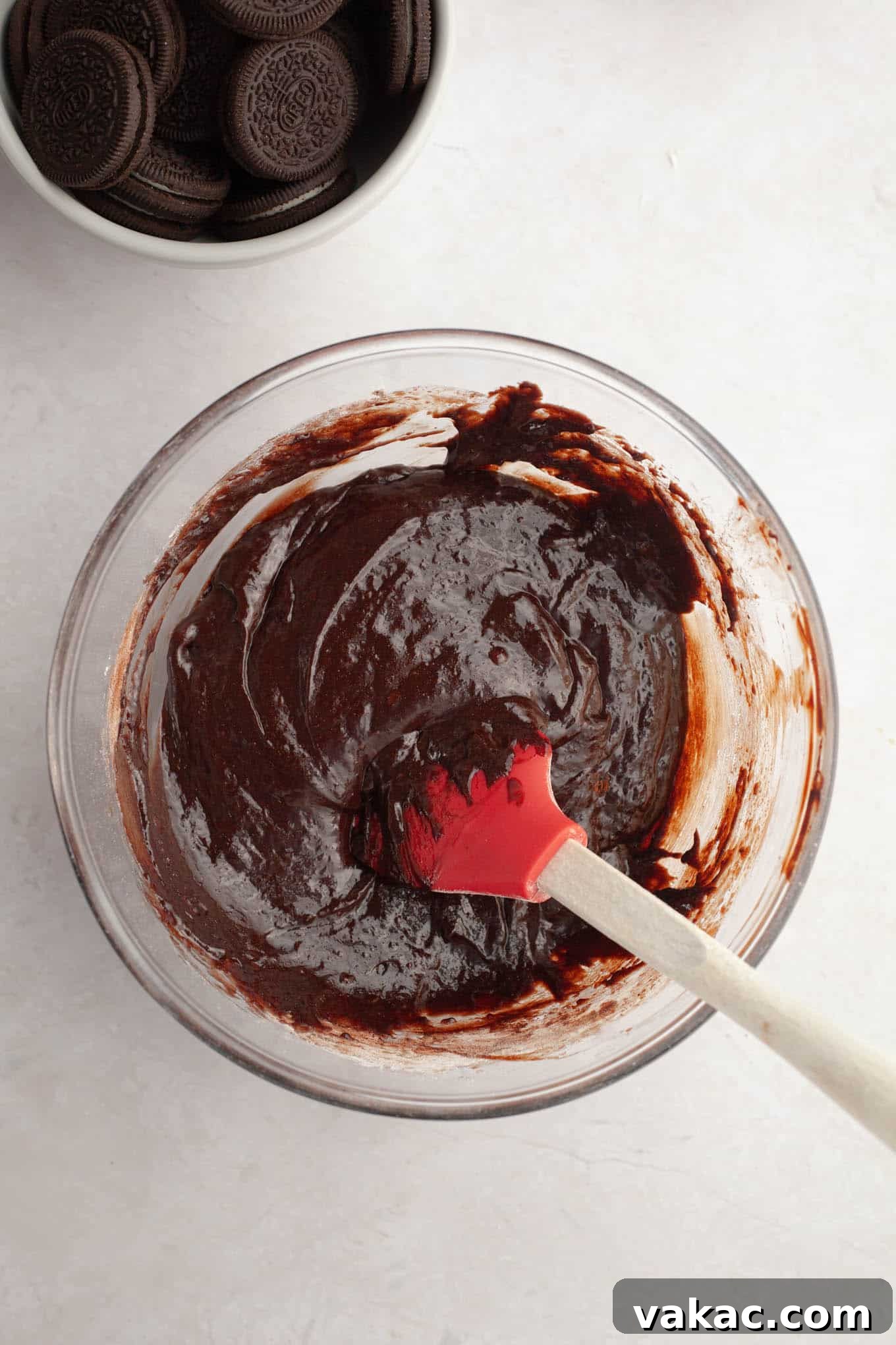 An overhead shot of glossy, smooth brownie batter being gently folded and stirred in a mixing bowl with a flexible spatula, showcasing its perfect consistency.