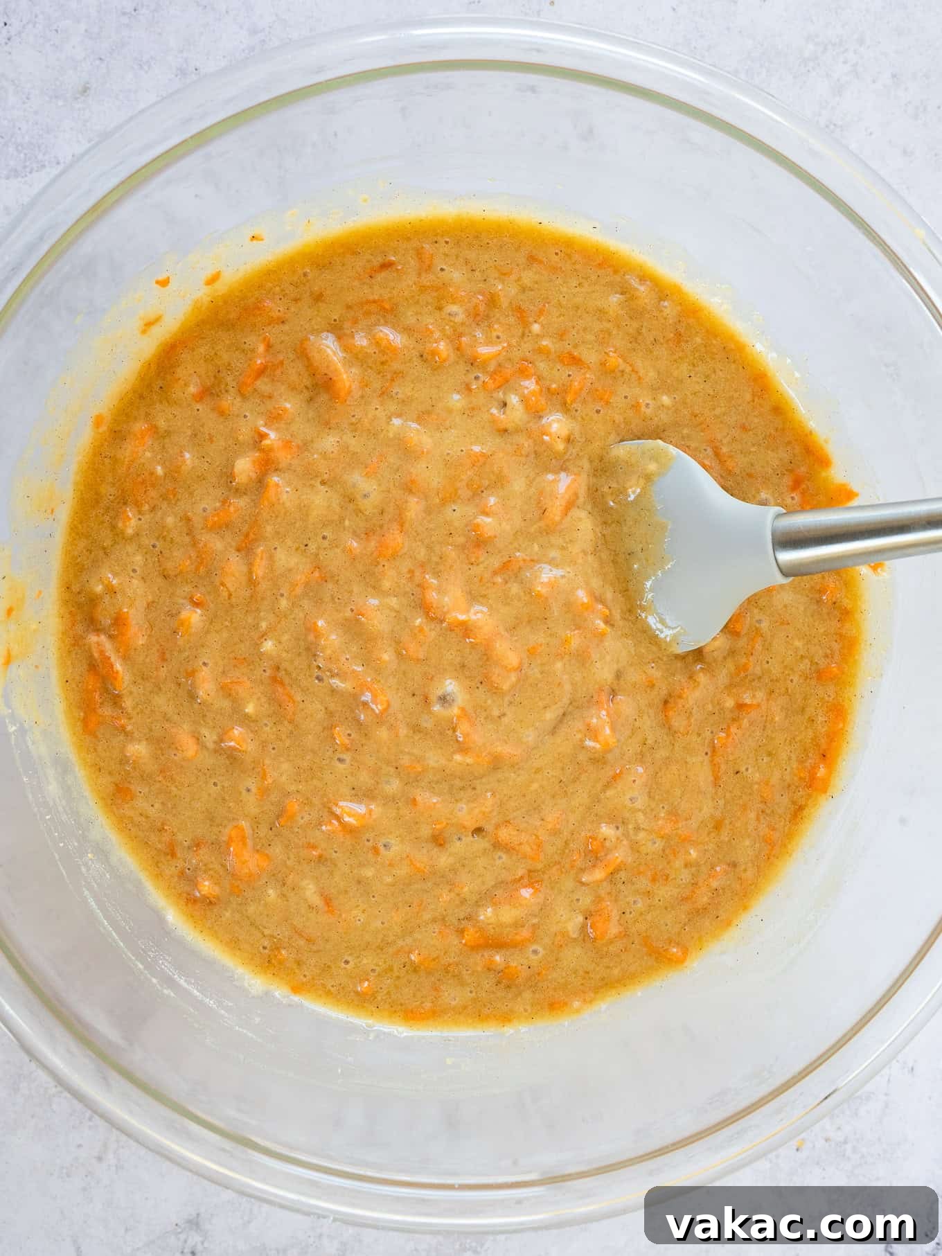 An overhead view of the carrot cake batter in a large mixing bowl with a rubber spatula.