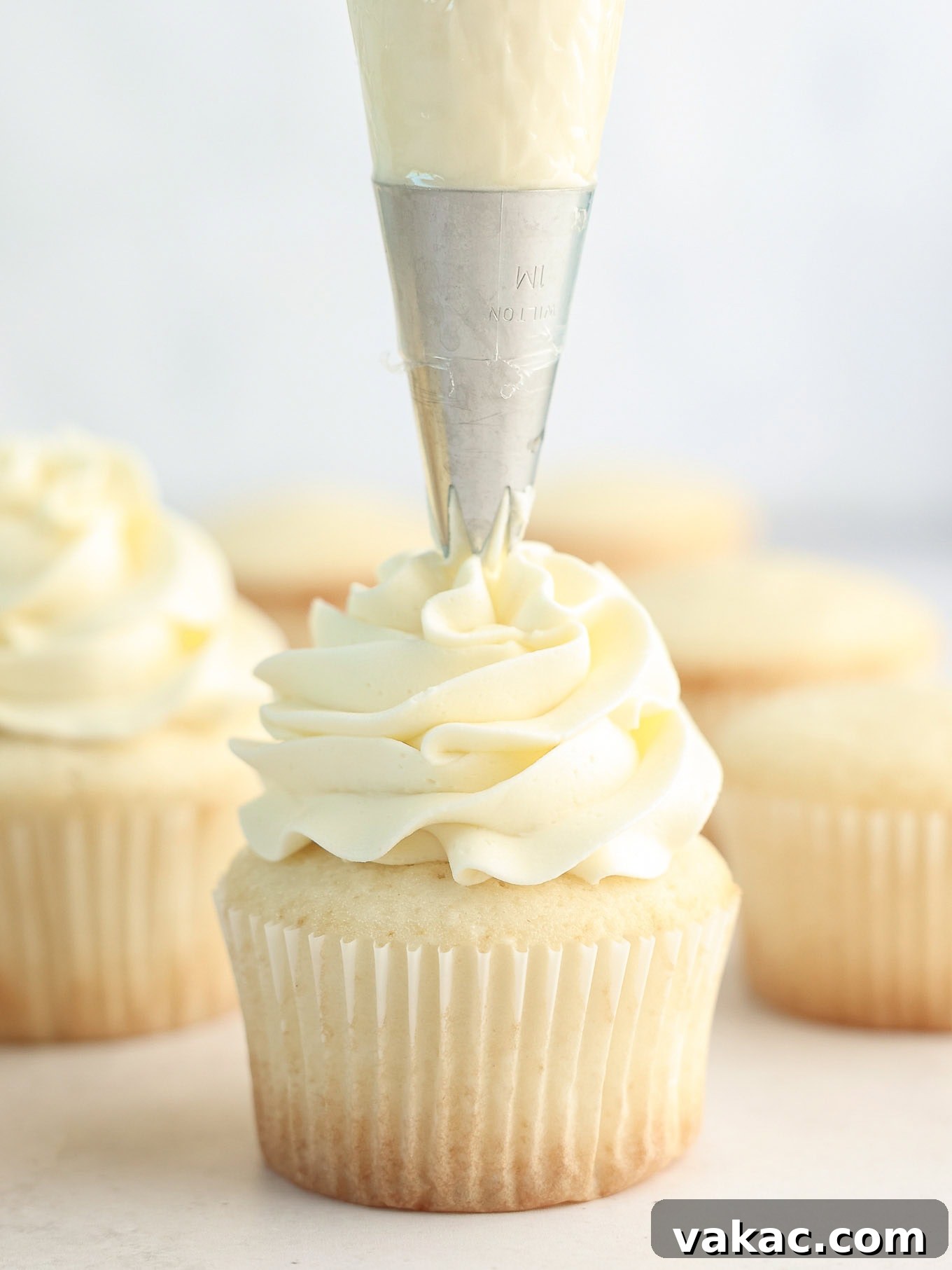 Fluffy White Cupcakes 11 Vanilla buttercream being expertly piped onto a freshly baked white cupcake, creating an elegant swirl.