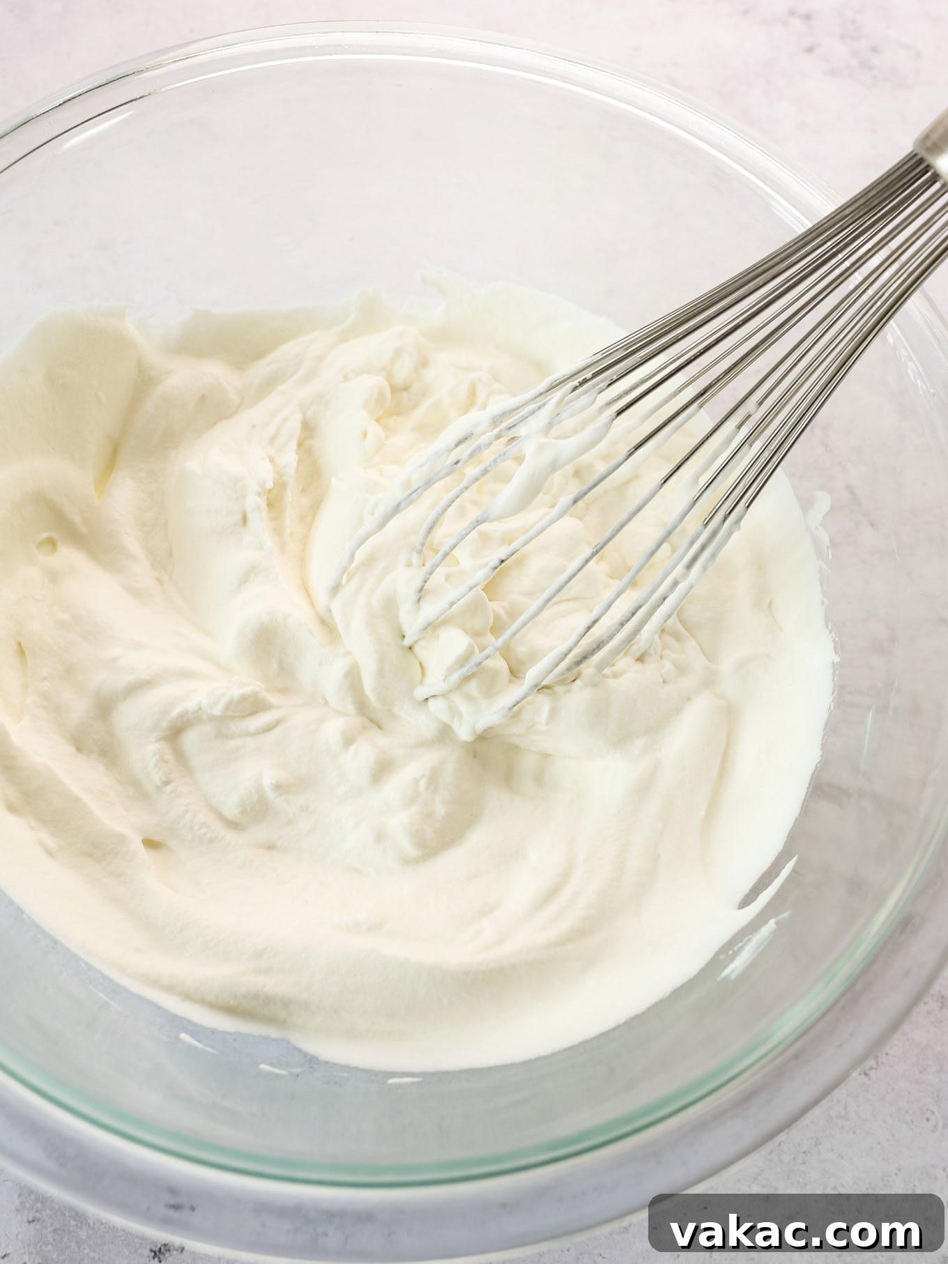Fluffy Cream Cheese Cloud 4 A whisk vigorously beating heavy whipping cream in a stainless steel bowl, creating soft, airy peaks, demonstrating the initial step in preparing whipped cream for frosting.