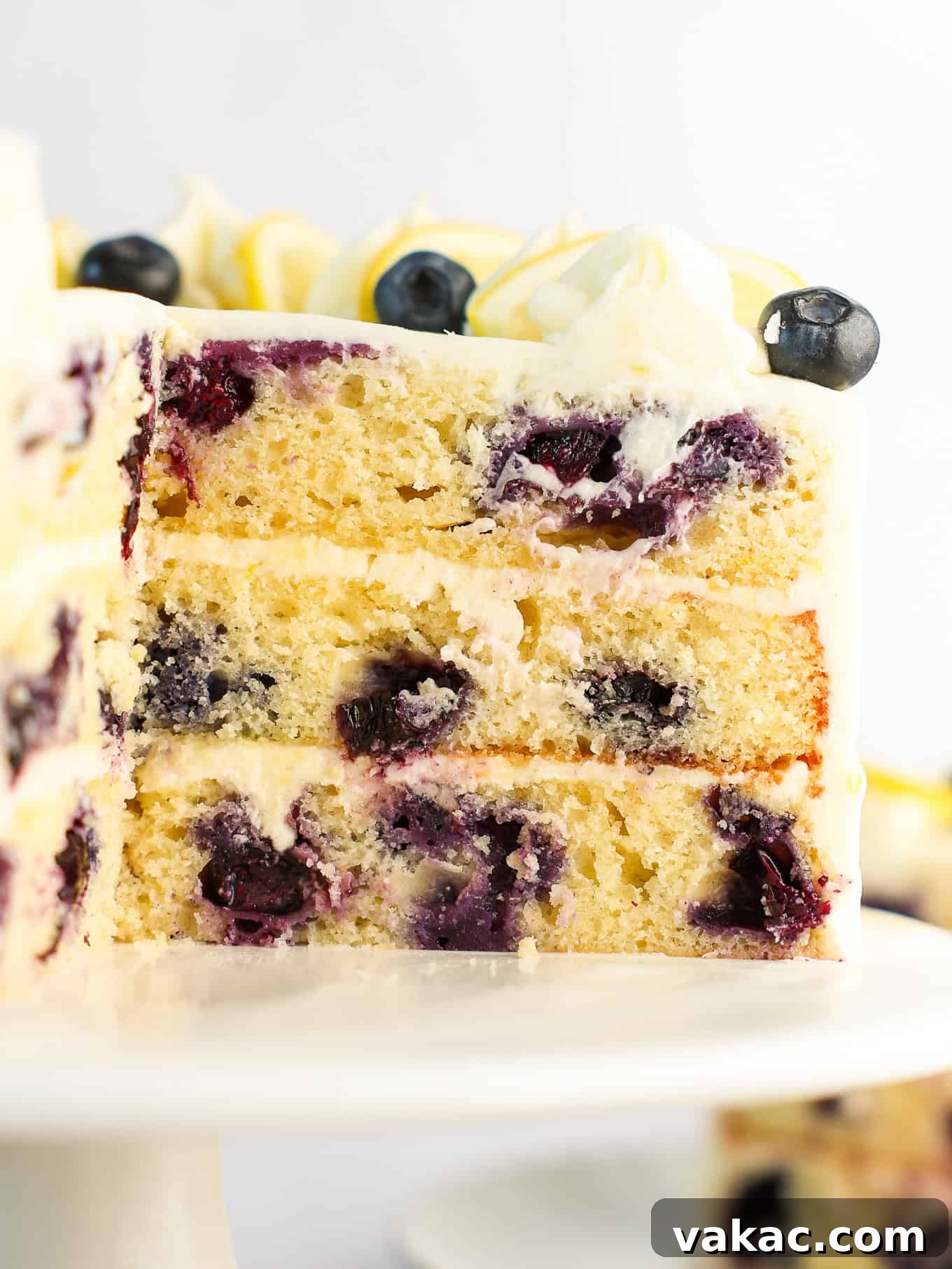 Sunshine Berry Cloud Cake 13 A slice of three-layer lemon blueberry cake on a white dessert plate, showing the moist interior with evenly distributed blueberries and layers of cream cheese frosting.
