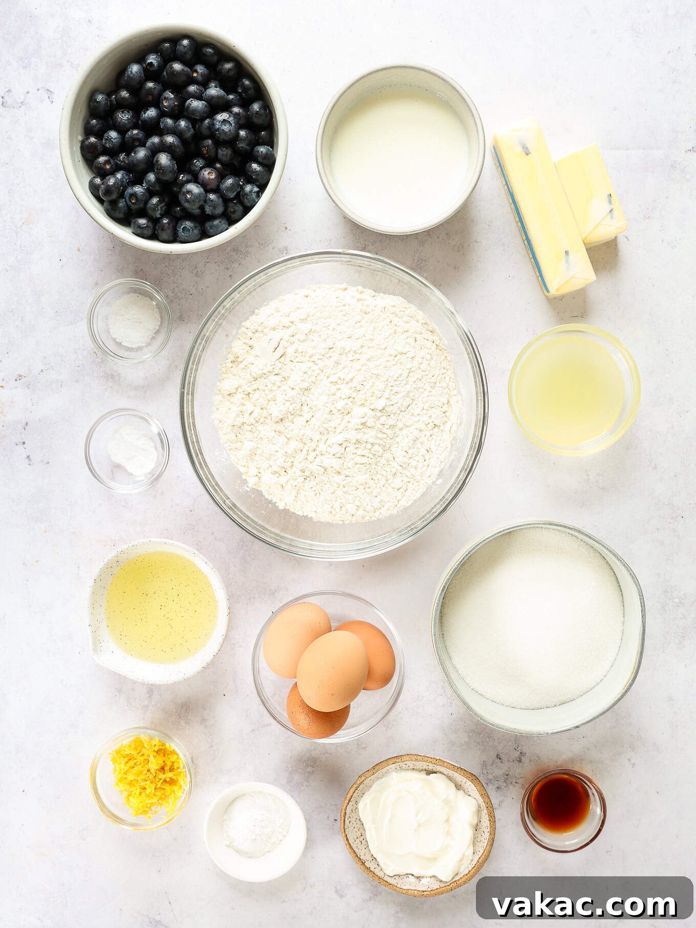Sunshine Berry Cloud Cake 3 A selection of fresh ingredients laid out on a kitchen counter, including lemons, blueberries, flour, butter, and dairy, essential for baking a delicious lemon blueberry cake.