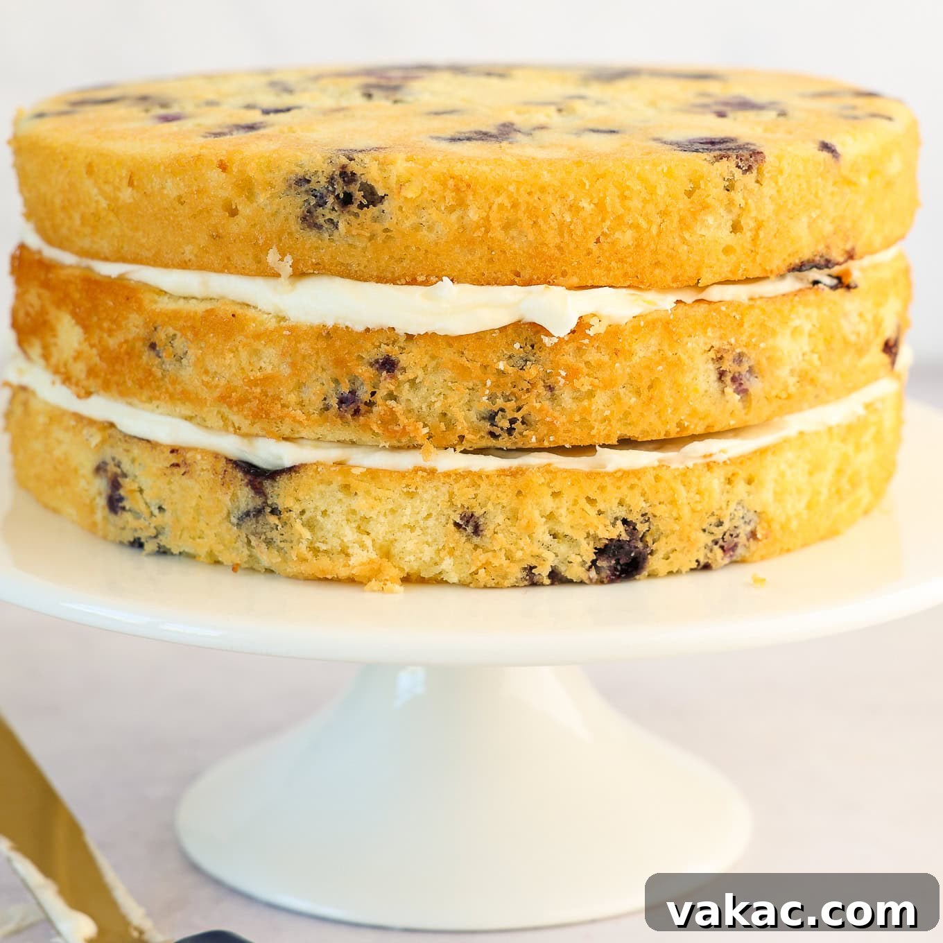 Sunshine Berry Cloud Cake 9 Three layers of baked lemon blueberry cake stacked with a generous amount of lemon cream cheese frosting between each layer, showing the cake assembly process.