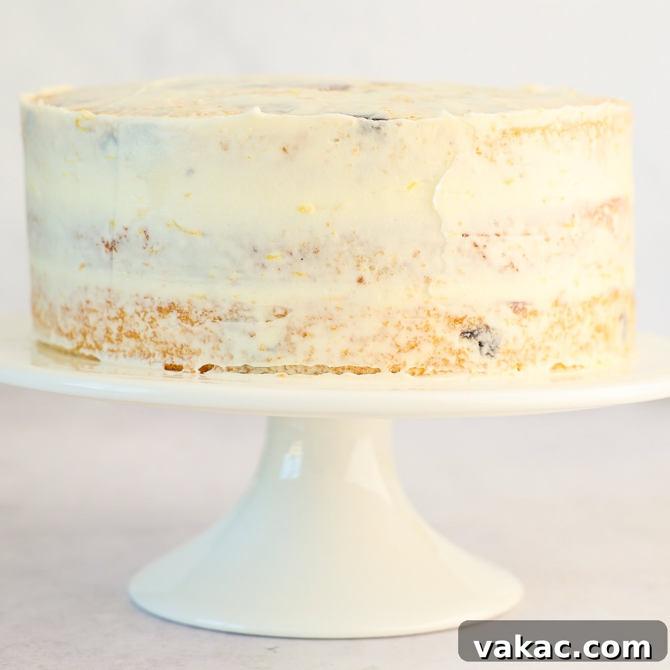 Sunshine Berry Cloud Cake 10 A three-layer cake covered with a thin, initial 'crumb coat' of frosting, preparing it for the final smooth layer.