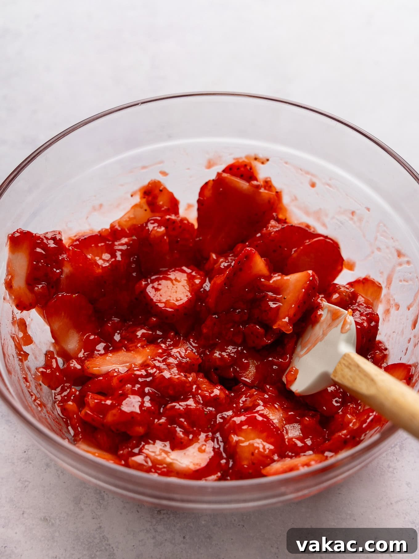 Strawberry Dream Cheesecake 5 Fresh strawberry topping in a mixing bowl with a spatula, showcasing its thick and vibrant texture.
