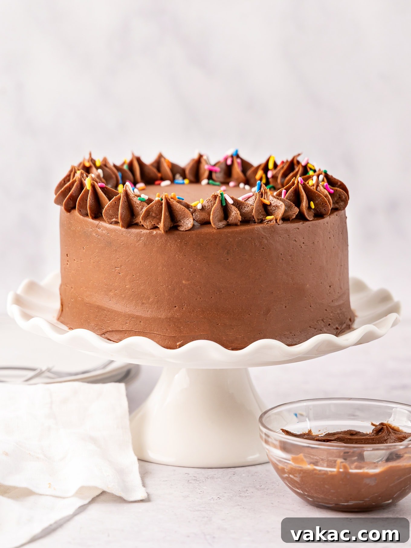 Mini Indulgence 2 A beautifully frosted two-layer 6-inch chocolate cake on a white cake stand, perfect for small gatherings.