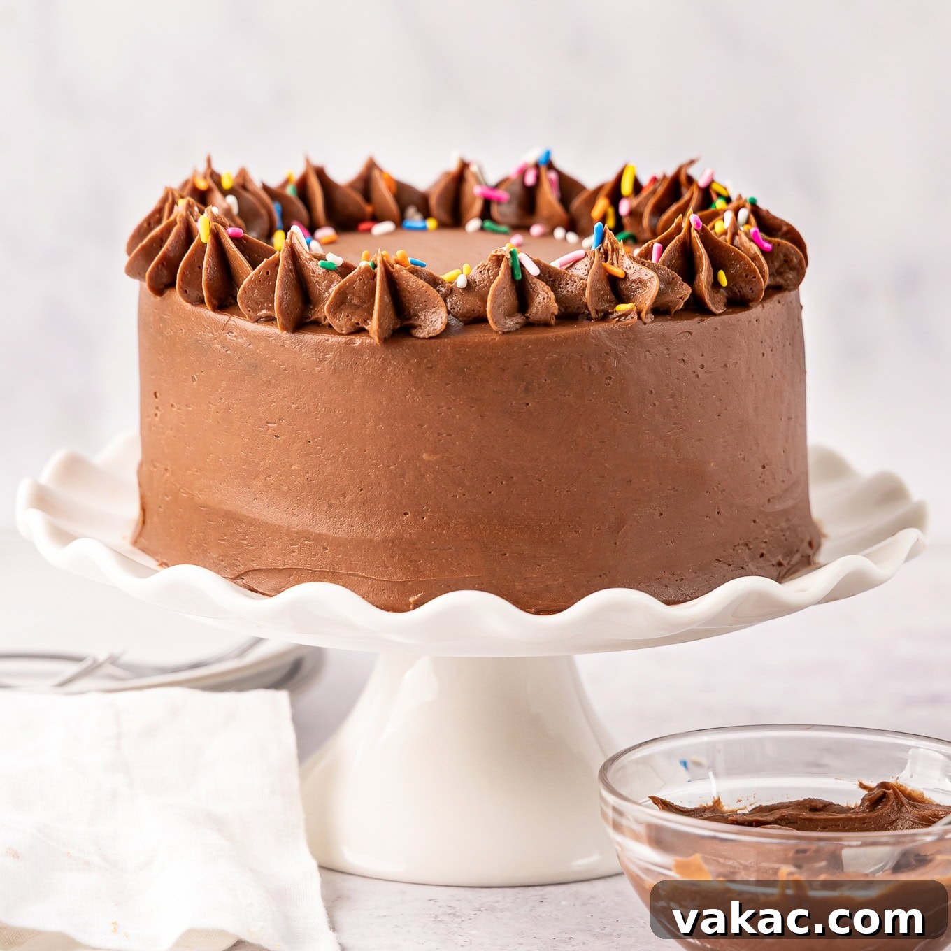Mini Indulgence 13 A small chocolate cake on a white cake stand, frosted and ready to serve.