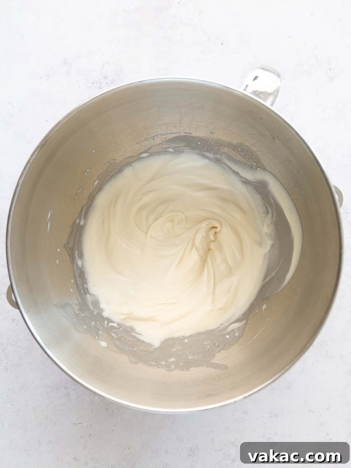 An overhead view of whipped cream with soft peaks in the bowl of a stand mixer, indicating the correct initial consistency.
