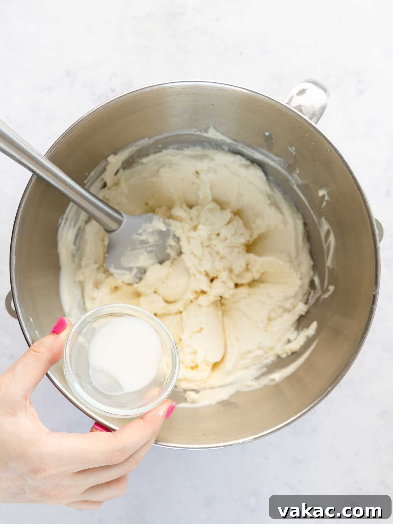 An overhead view of milk being added to curdled mascarpone frosting, illustrating a repair step.