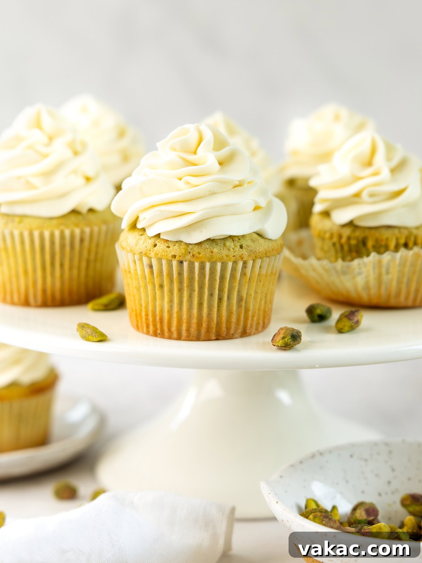 Pistachio cupcakes with mascarpone frosting on a cake stand, highlighting the frosting's ability to hold its shape.
