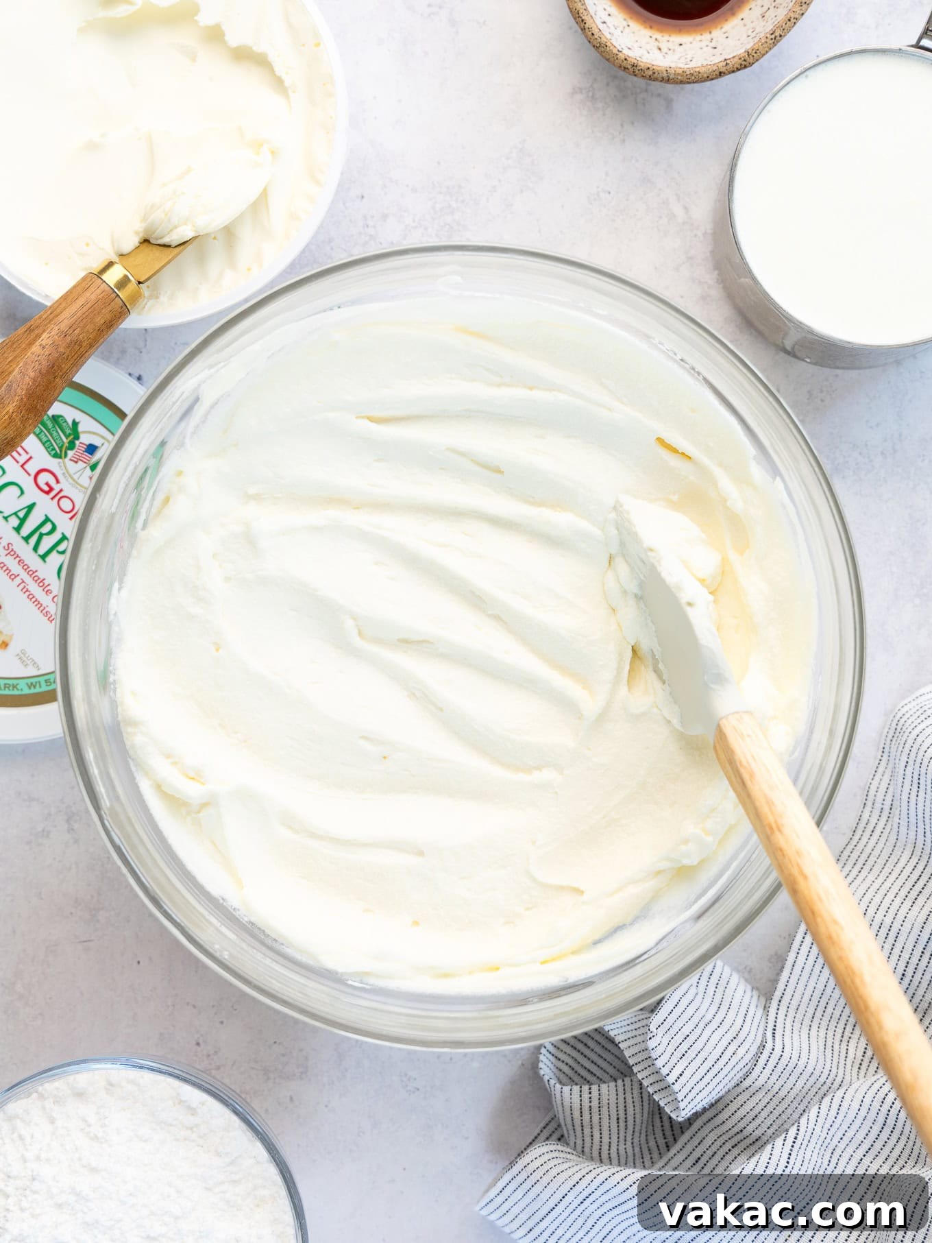 A bowl of mascarpone frosting with a rubber spatula in it, showing its smooth consistency.