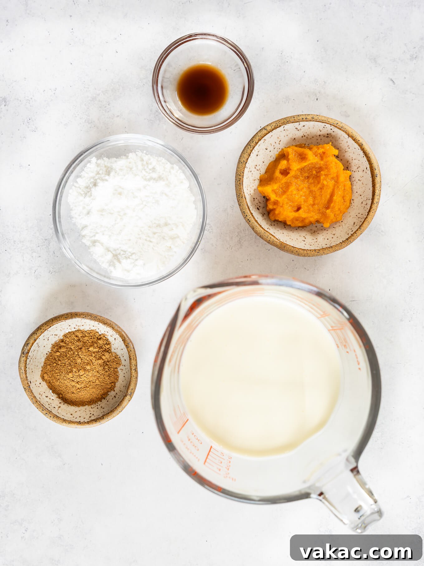 All the essential ingredients neatly arranged on a counter for preparing delicious pumpkin spice whipped cream: heavy cream, powdered sugar, pumpkin puree, pumpkin pie spice, and vanilla extract.