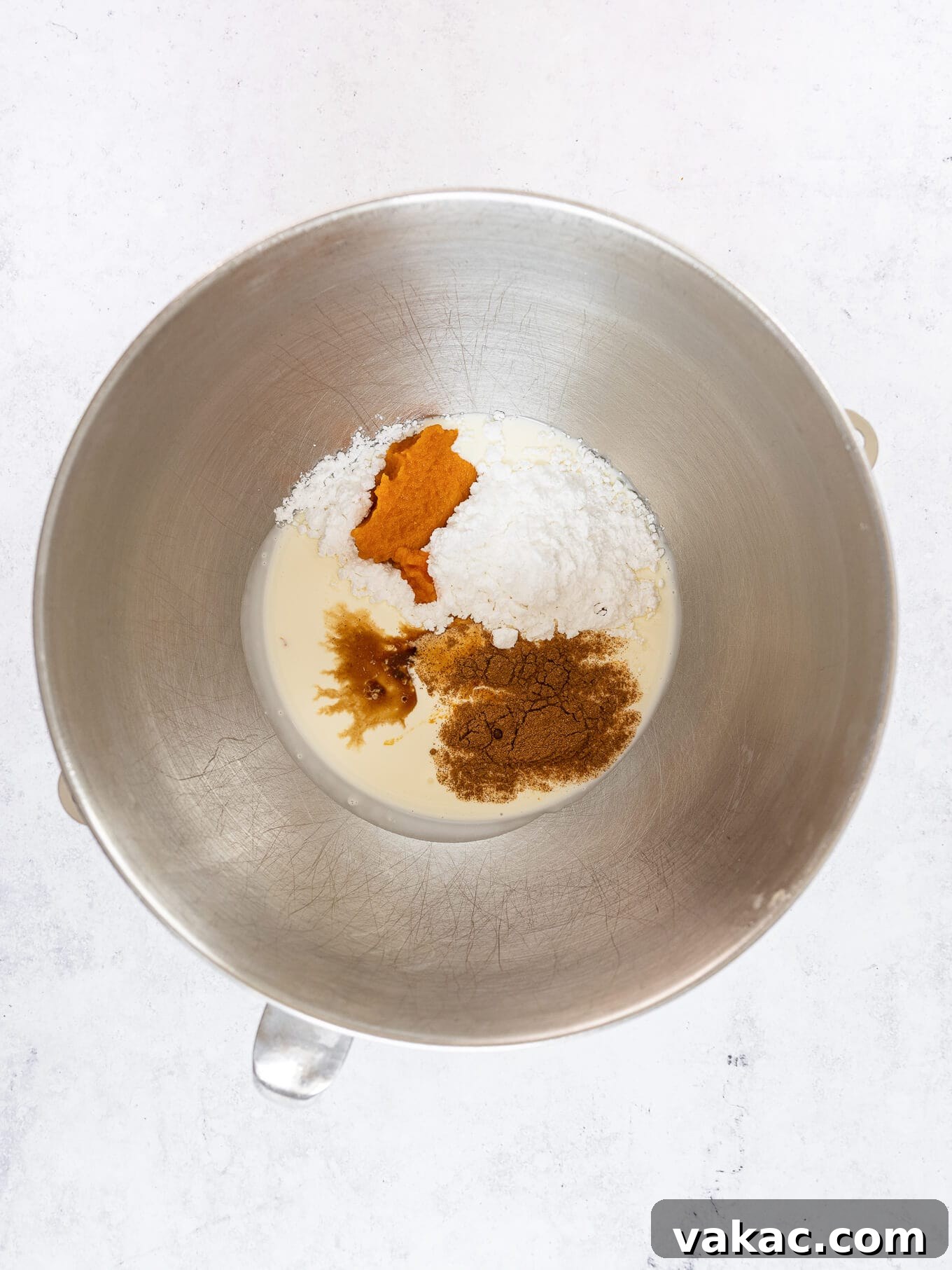 Heavy whipping cream, pumpkin puree, pumpkin pie spice, and vanilla extract are carefully measured and combined in a large mixing bowl, ready for whipping.