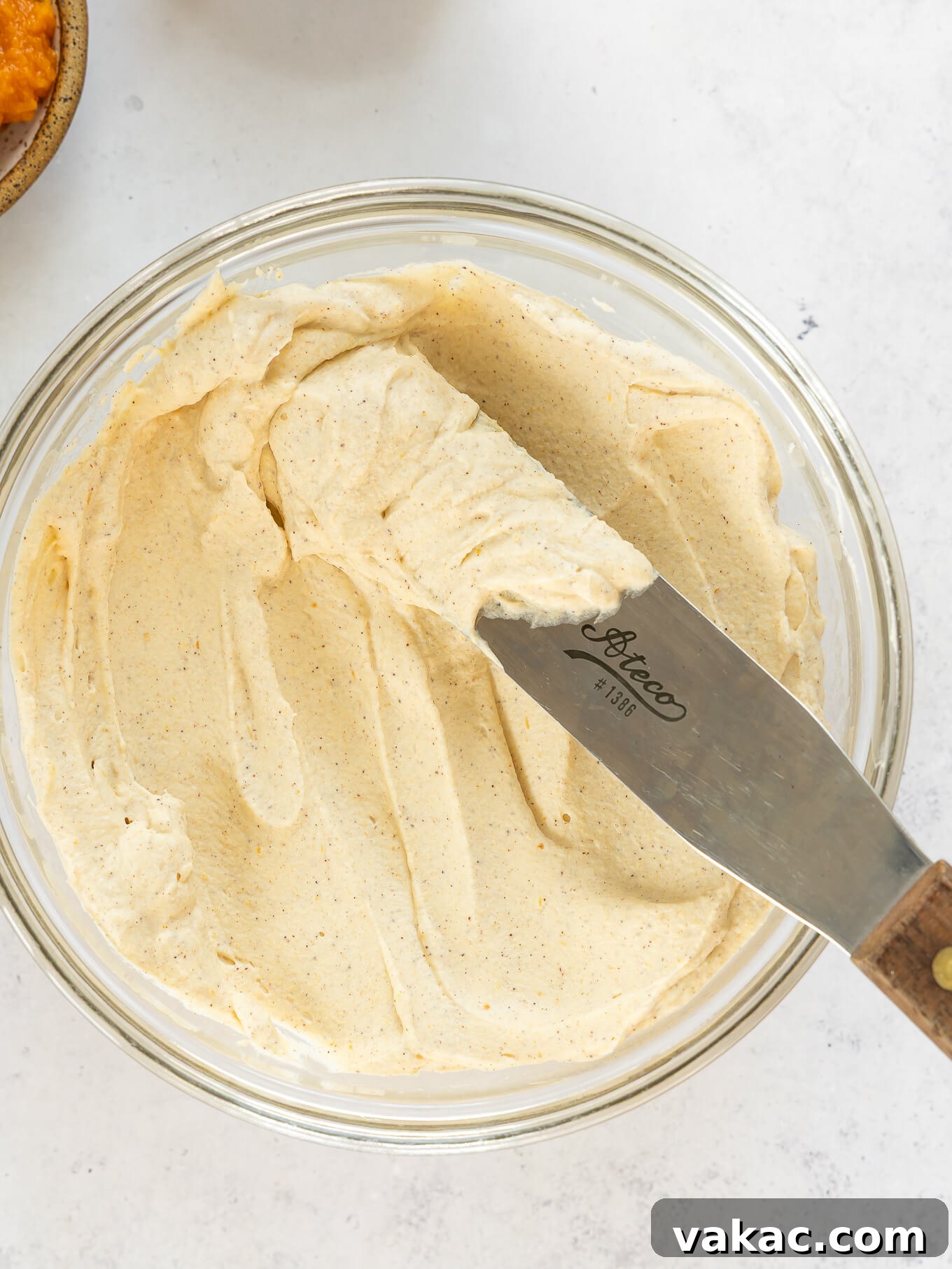 A beautifully textured bowl of pumpkin whipped cream, accompanied by an offset spatula, inviting you to serve this delightful topping.