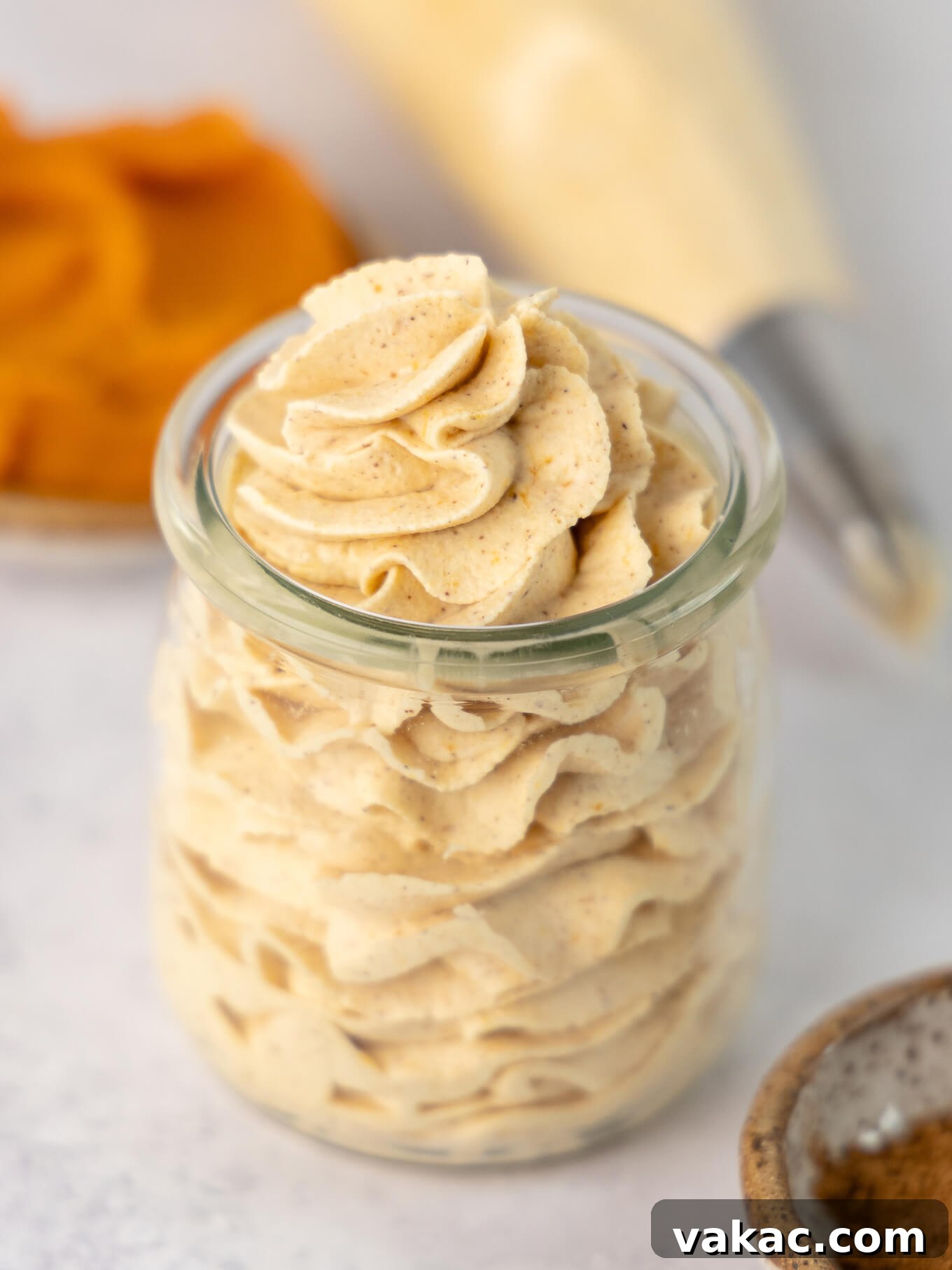 A charming clear glass jar filled with perfectly piped pumpkin spiced whipped cream, showcasing its beautiful texture.