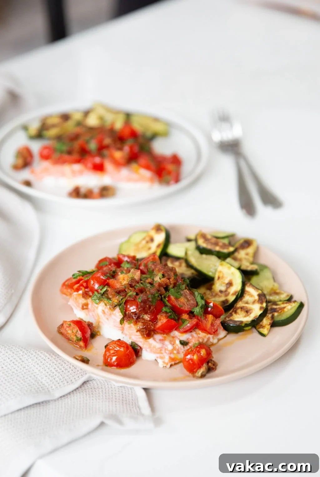 Mediterranean Baked Salmon with Sun-Dried Tomato Aioli 2 Two servings of perfectly baked salmon, each topped with a rich sun-dried tomato aioli, accompanied by vibrant zucchini slices on elegant pink and white plates.