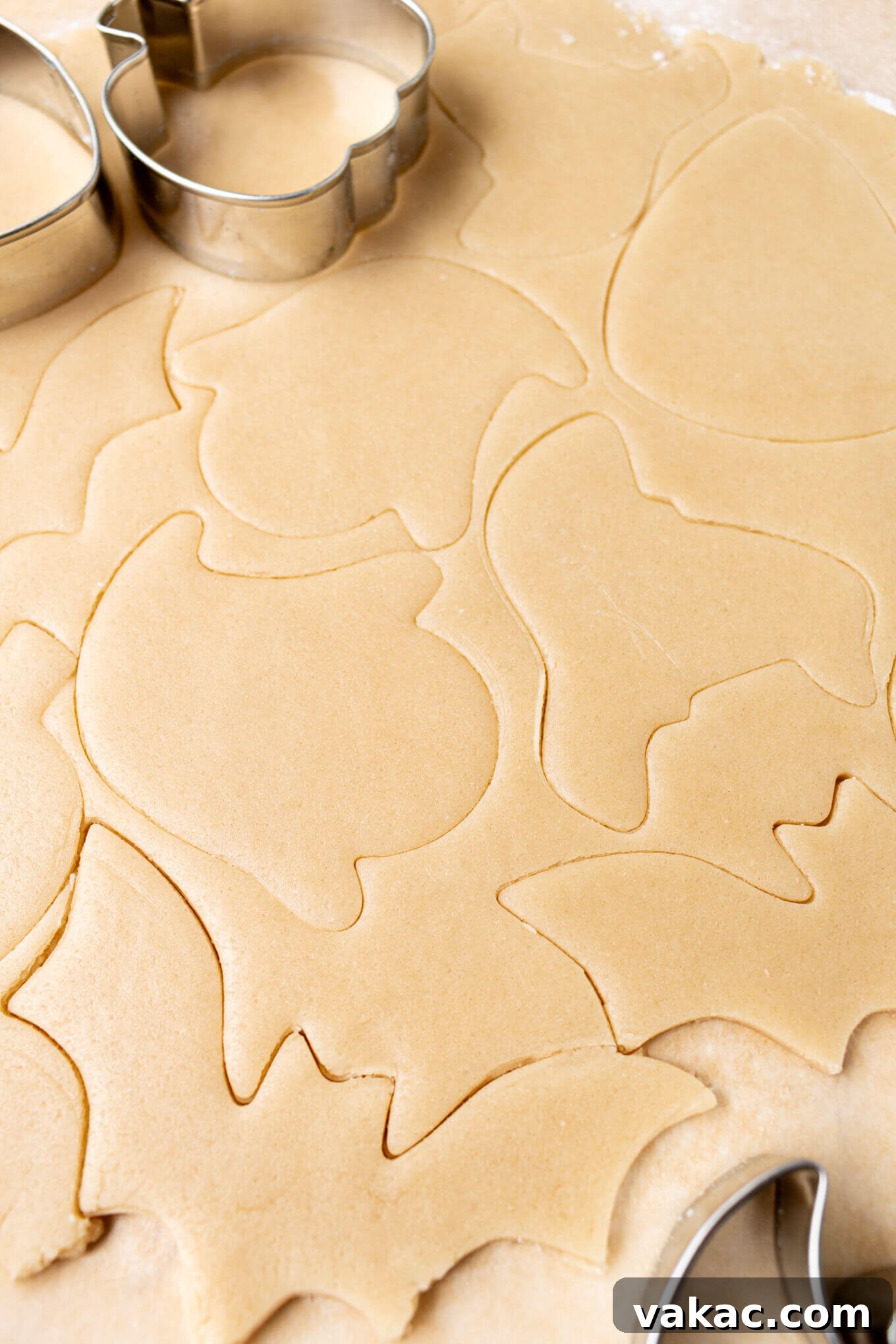 Ghoulishly Good Sugar Cookies 4 Sugar cookie dough rolled out between two sheets of parchment paper and cut into Halloween shapes using various cookie cutters.