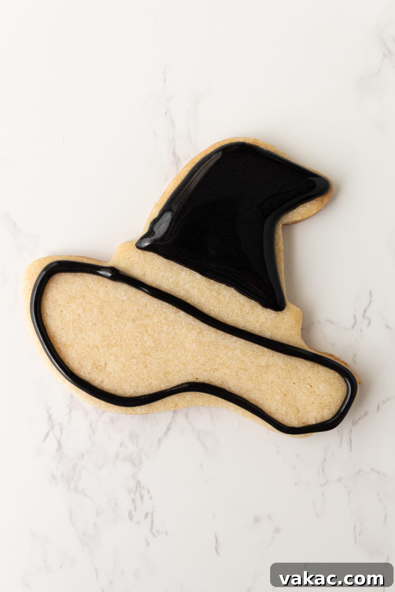 Ghoulishly Good Sugar Cookies 7 A detailed image of a witch's hat sugar cookie being decorated with royal icing, showing one section outlined and filled, and another section just outlined.