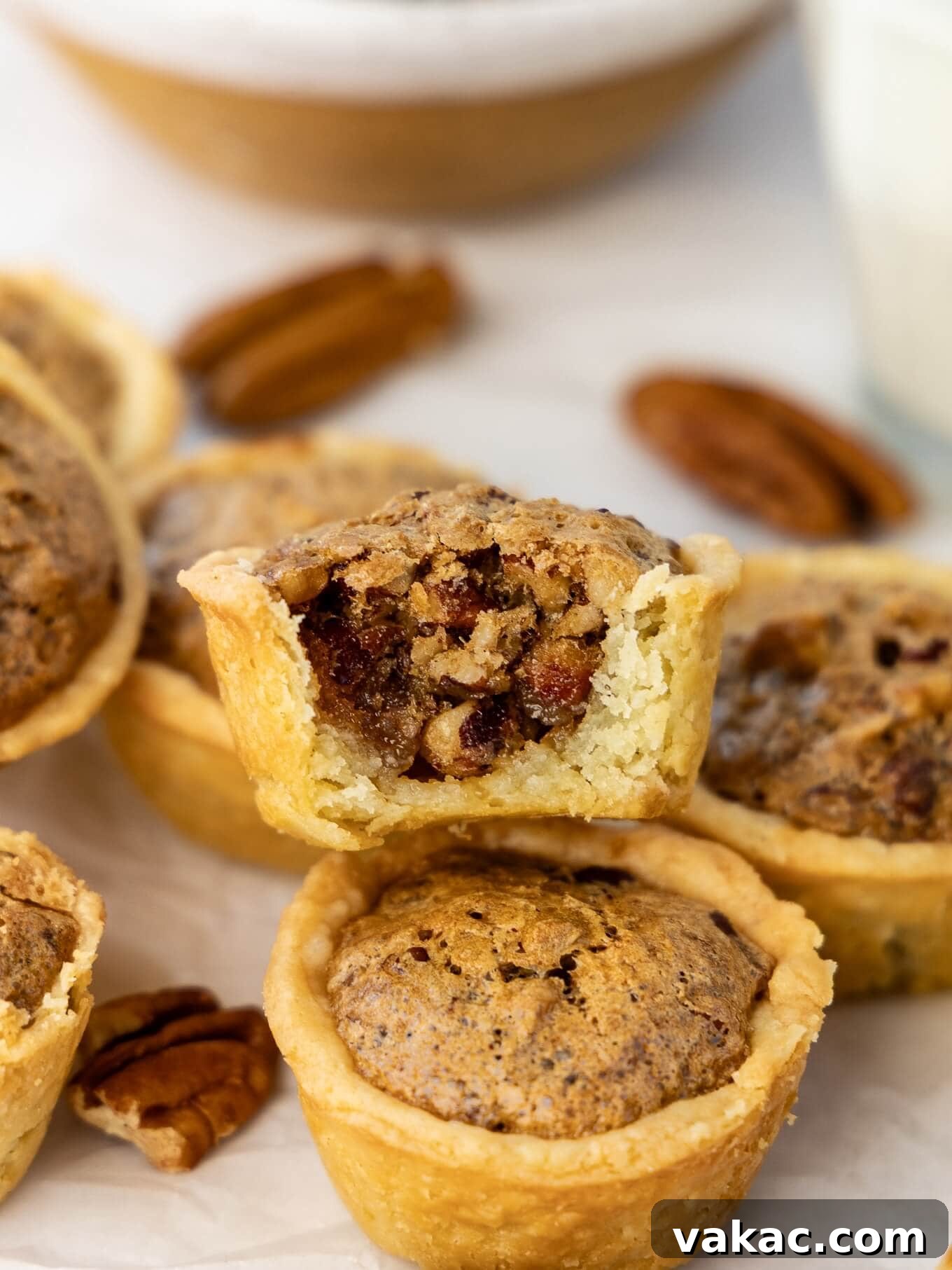 Southern Pecan Treasures 2 A beautifully arranged pile of golden-brown pecan tassies, with one at the top showing a delicious bite taken out, revealing the gooey pecan filling.