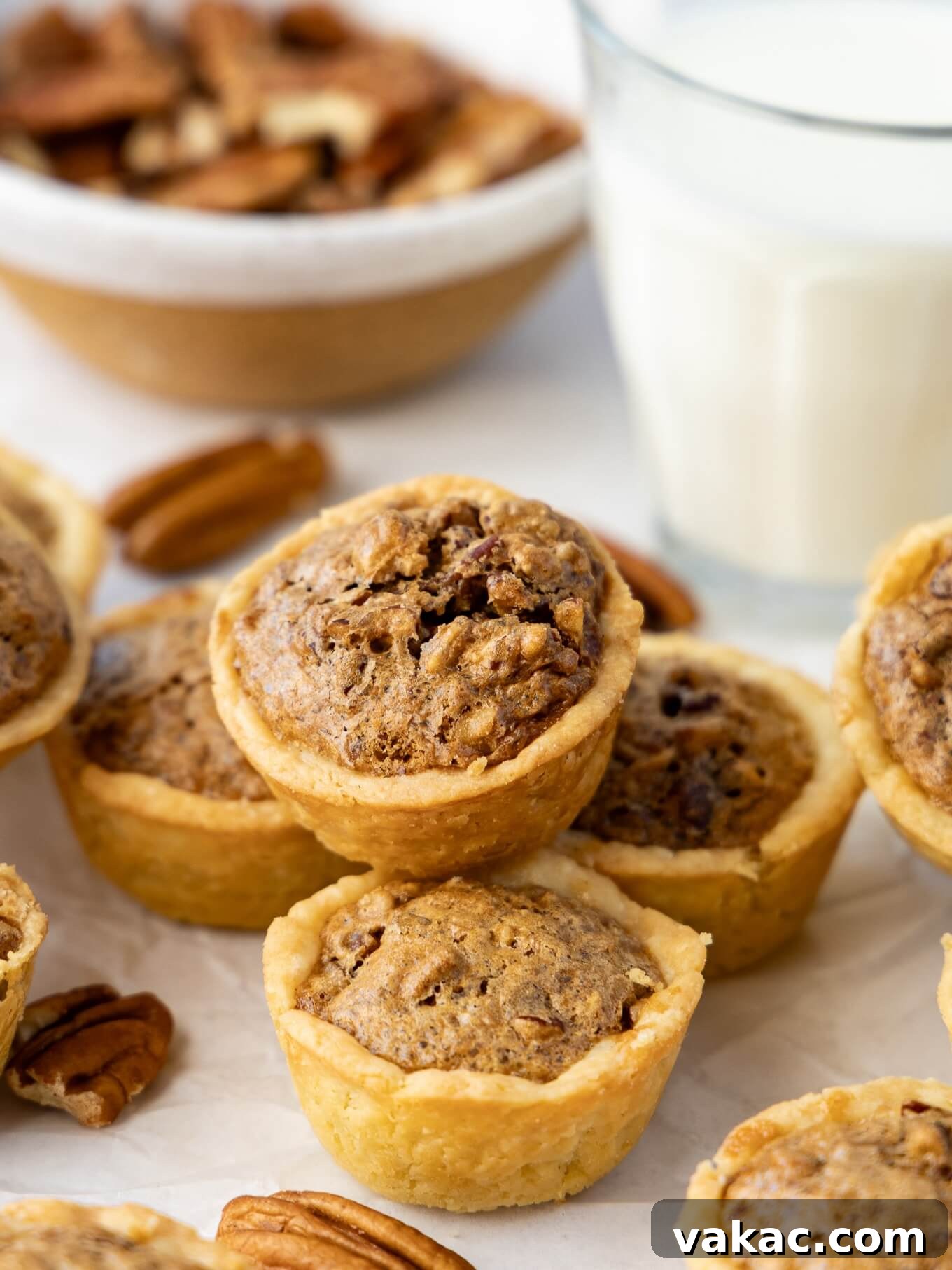 Southern Pecan Treasures 8 A charming pile of golden-brown pecan tassies, perfectly baked, with whole and chopped pecans scattered around them, emphasizing their key ingredient.